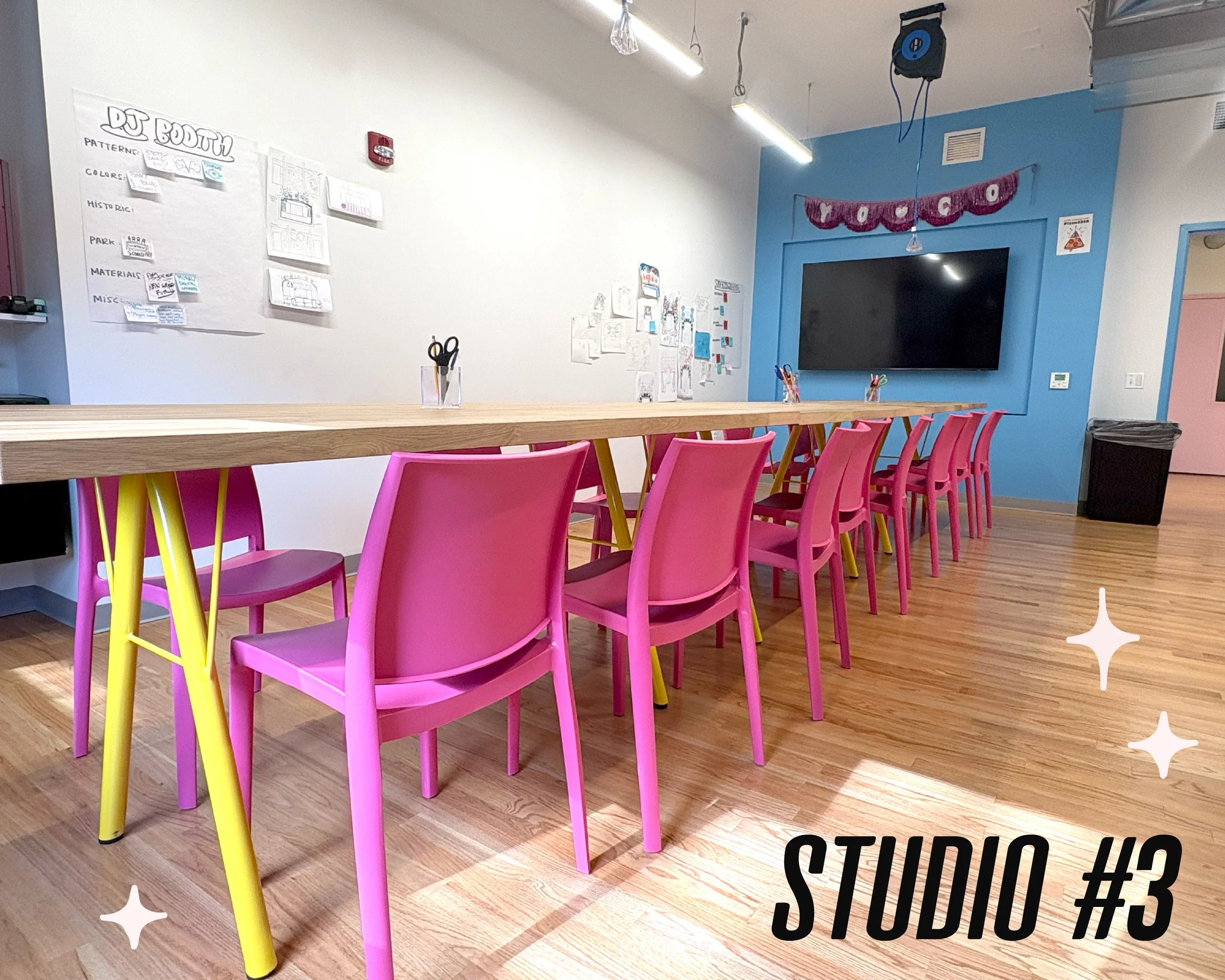 Graphic text that reads "Studio #3" is seen over an image of another workspace. The space is brught and has muliple tables with pink chairs. A blue accent wall and screen are visible.