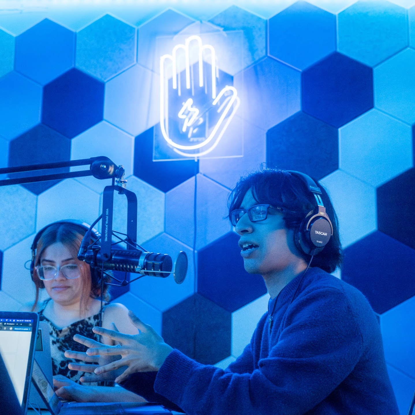 Two young people sit in a radio studio, engaged in conversation.