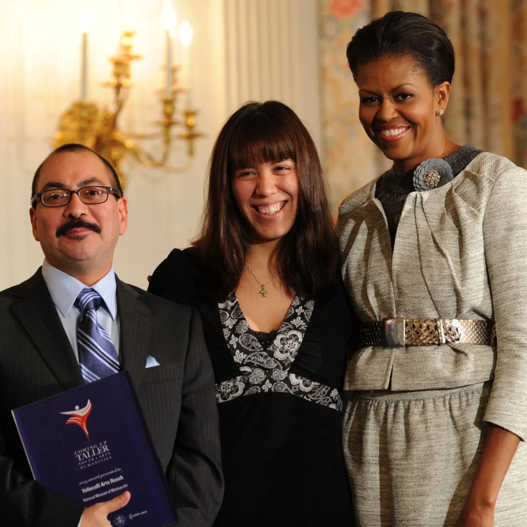 Two adults pose with former first lady, Michelle Obama, after recieving the National Arts and Humanities Youth Program Award.