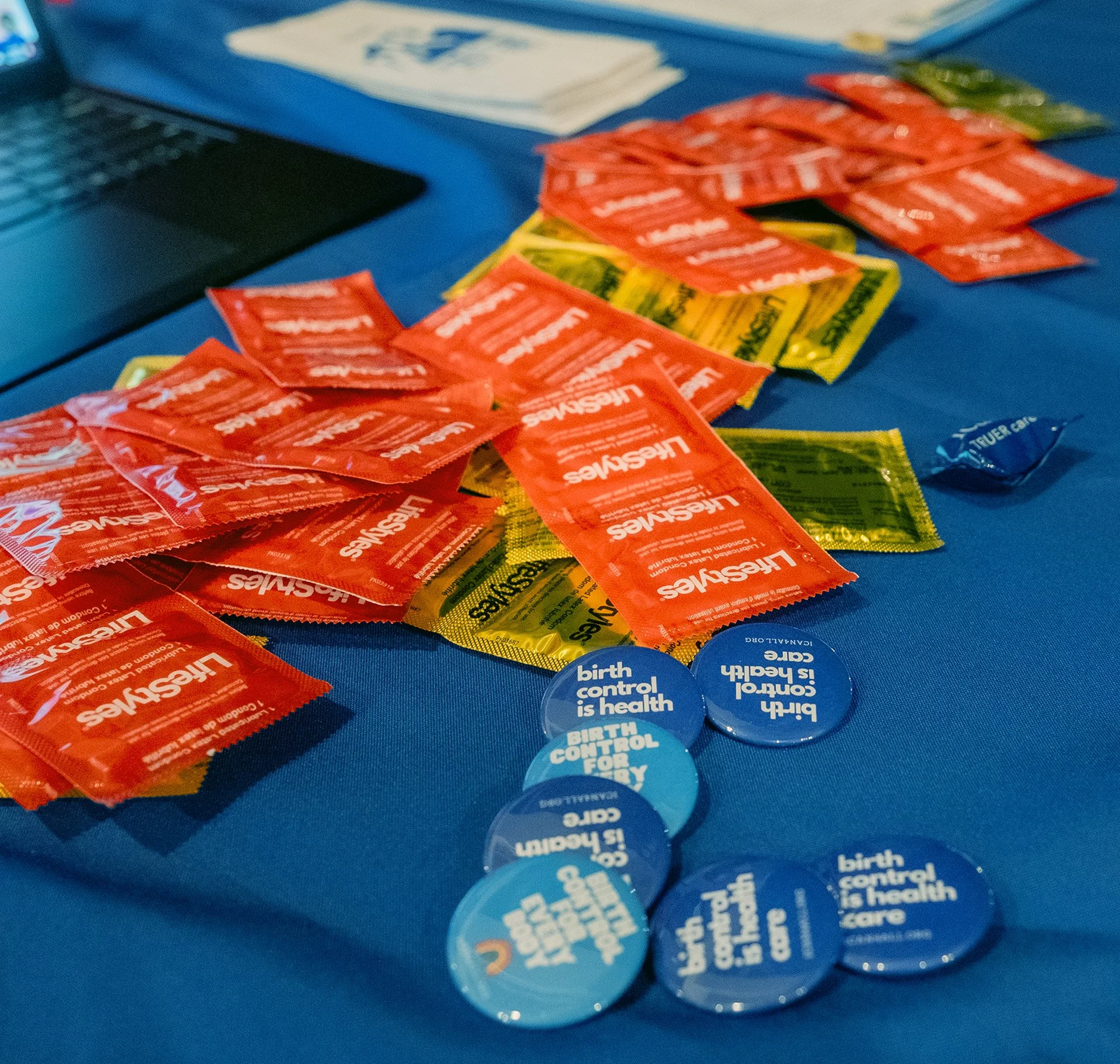 Assorted packets of condoms and buttons with messages promoting sexual health and birth control on a blue table.