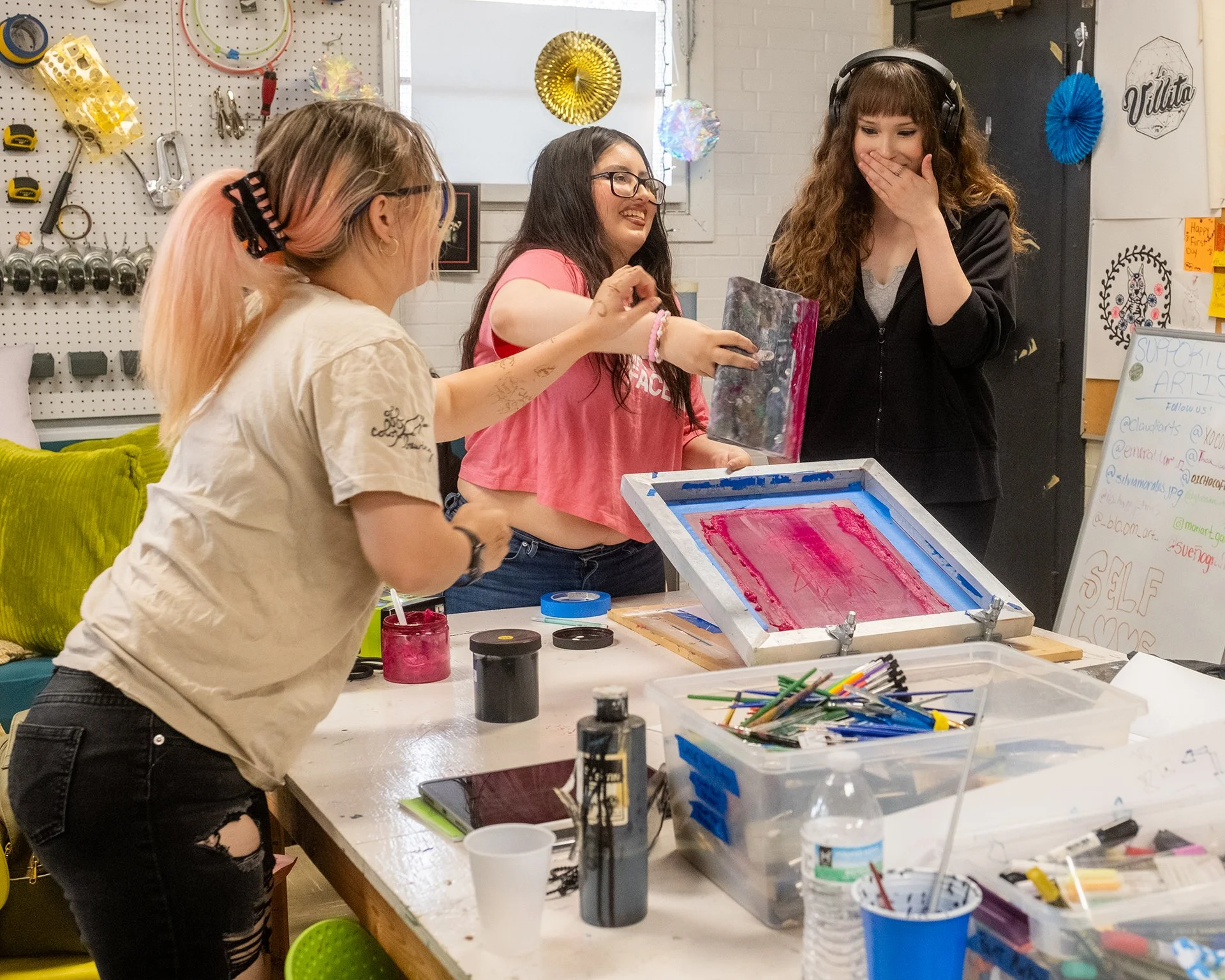 Three young people share a laugh as they work on a screen-printing project.