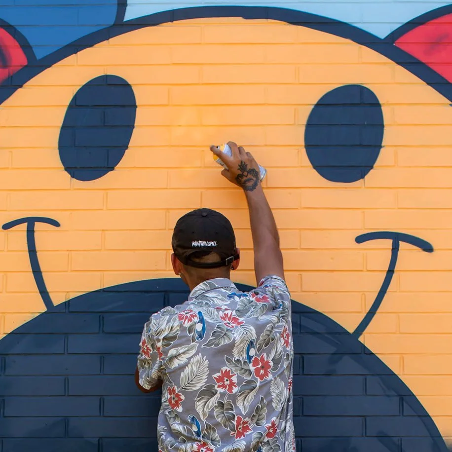 An young person uses a spray paint can to contribute to an outdoor graffiti art piece.