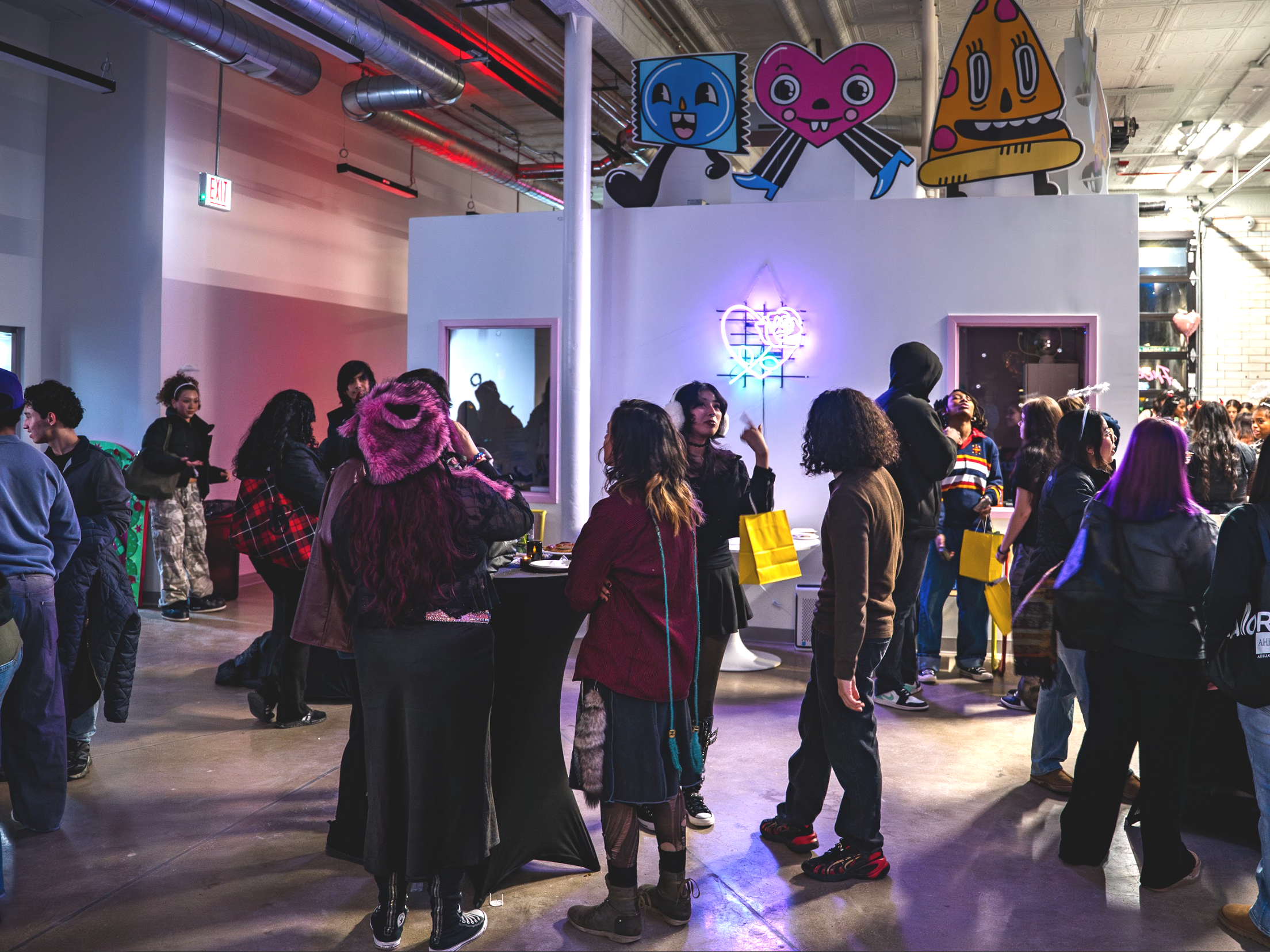 Groups of young people gather in the interior of the Yollocalli firehouse. The walls are white but are decorated with colorful lights, and character standees.