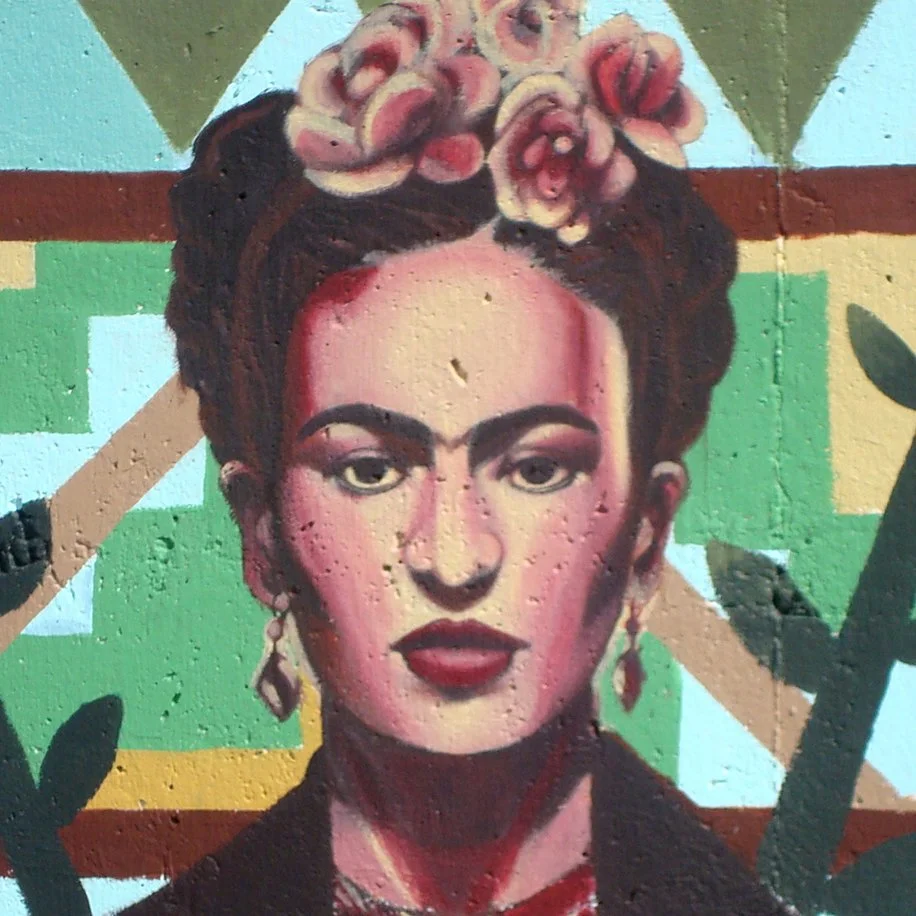A painted mural depiction of Frida Khalo. In the painting she wears flowers in her hair and is surounded by geometric patterns.
