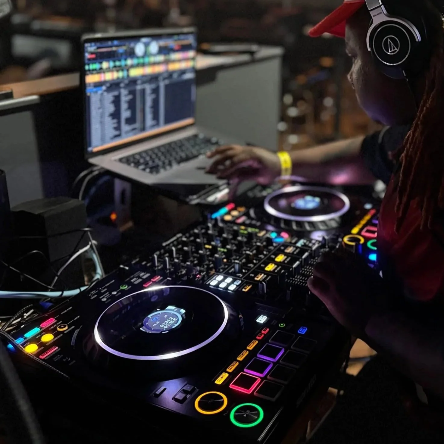 A young person navigates audio production tools on a laptop. In the foreground, two turntables light up in various colors.