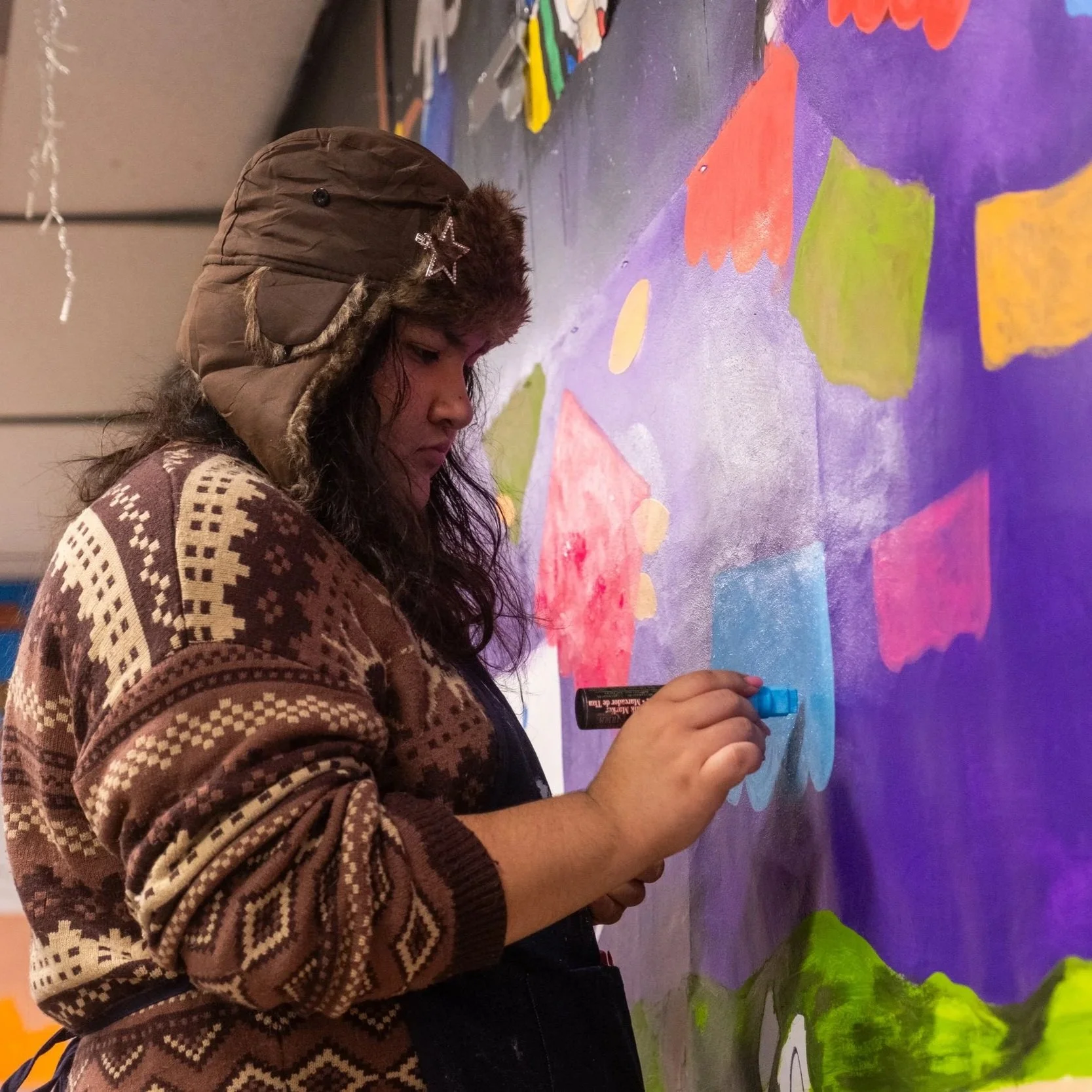 A young person uses a paint pen to contribute to a mural.
