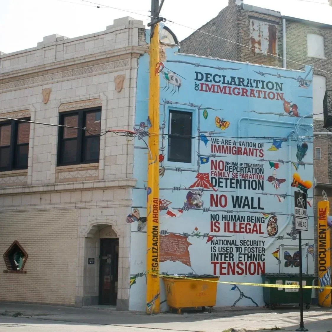 A large mural on the side of a building with a blue background and barbed wire illustrations. The mural has the title "Declaration of Immigration" and lists statements promoting immigrant rights, opposing detention, deportation, walls, and dehumanization, and emphasizing the importance of human beings and national security.
