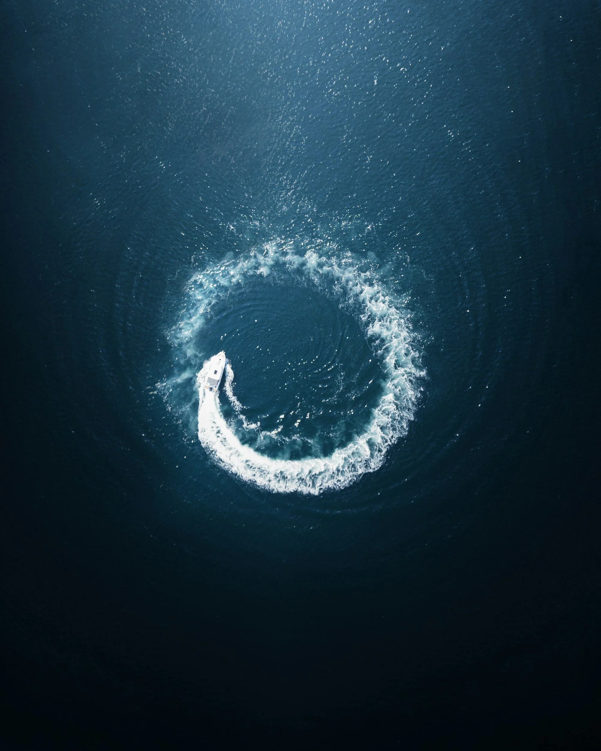 An aerial view of a boat creating a spiral wake in the water.