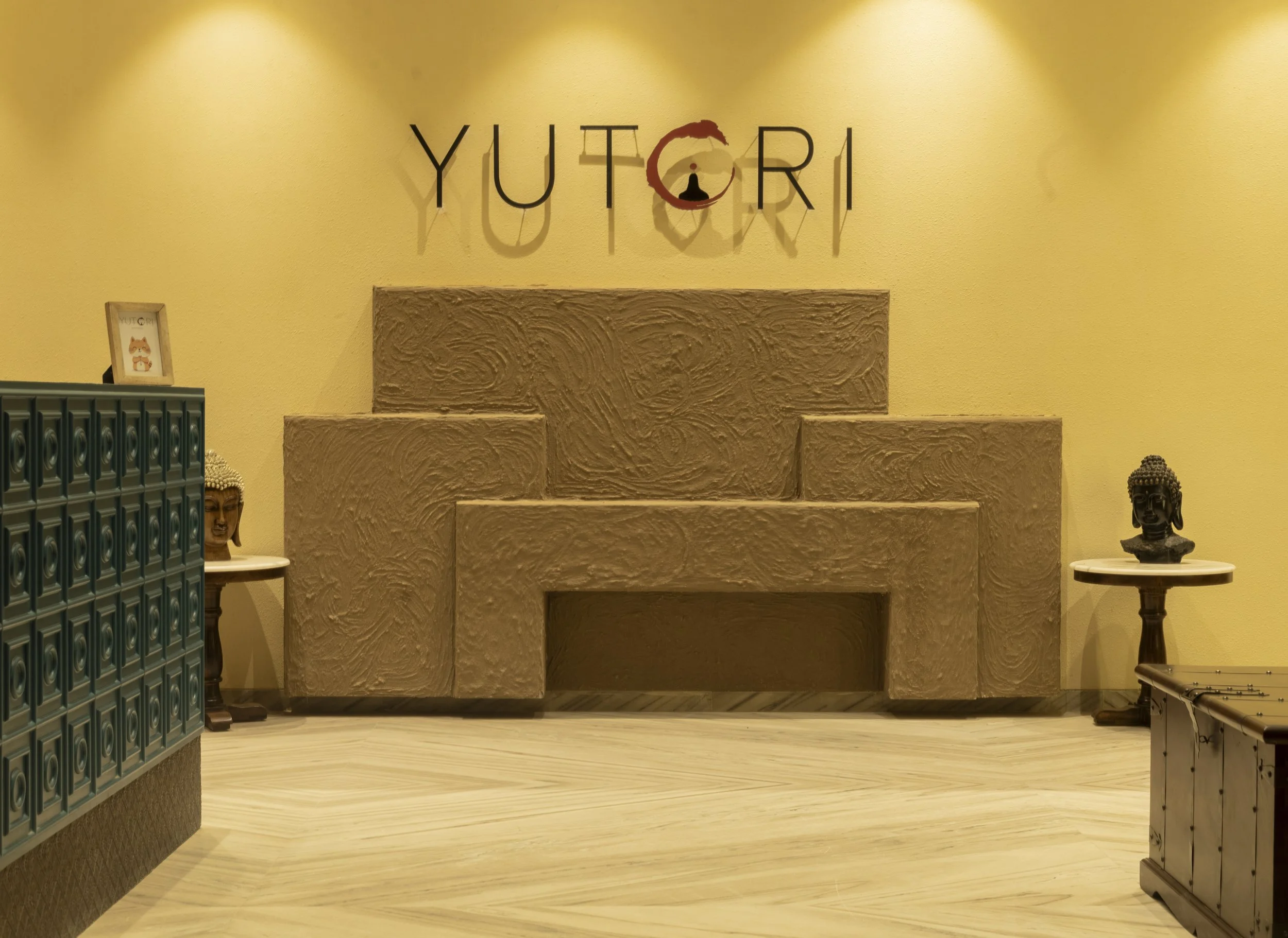 Decorative fireplace with Buddha statues on round tables on each side, yellow wall with the word 'YUTCRI' in black letters, and a framed picture of a fox on a green cabinet.