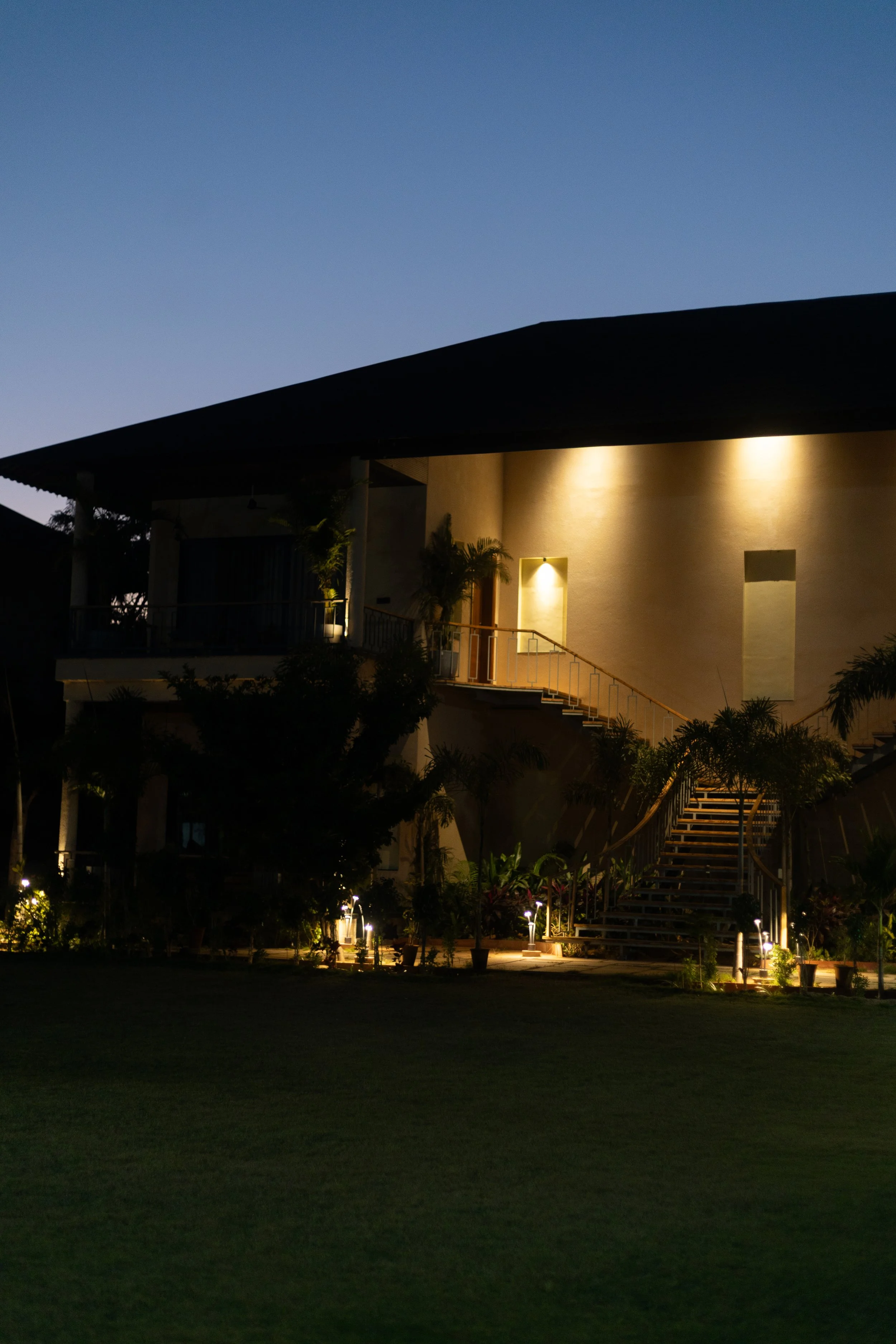 A modern house at night with exterior lighting, staircase, and tropical plants in the garden.