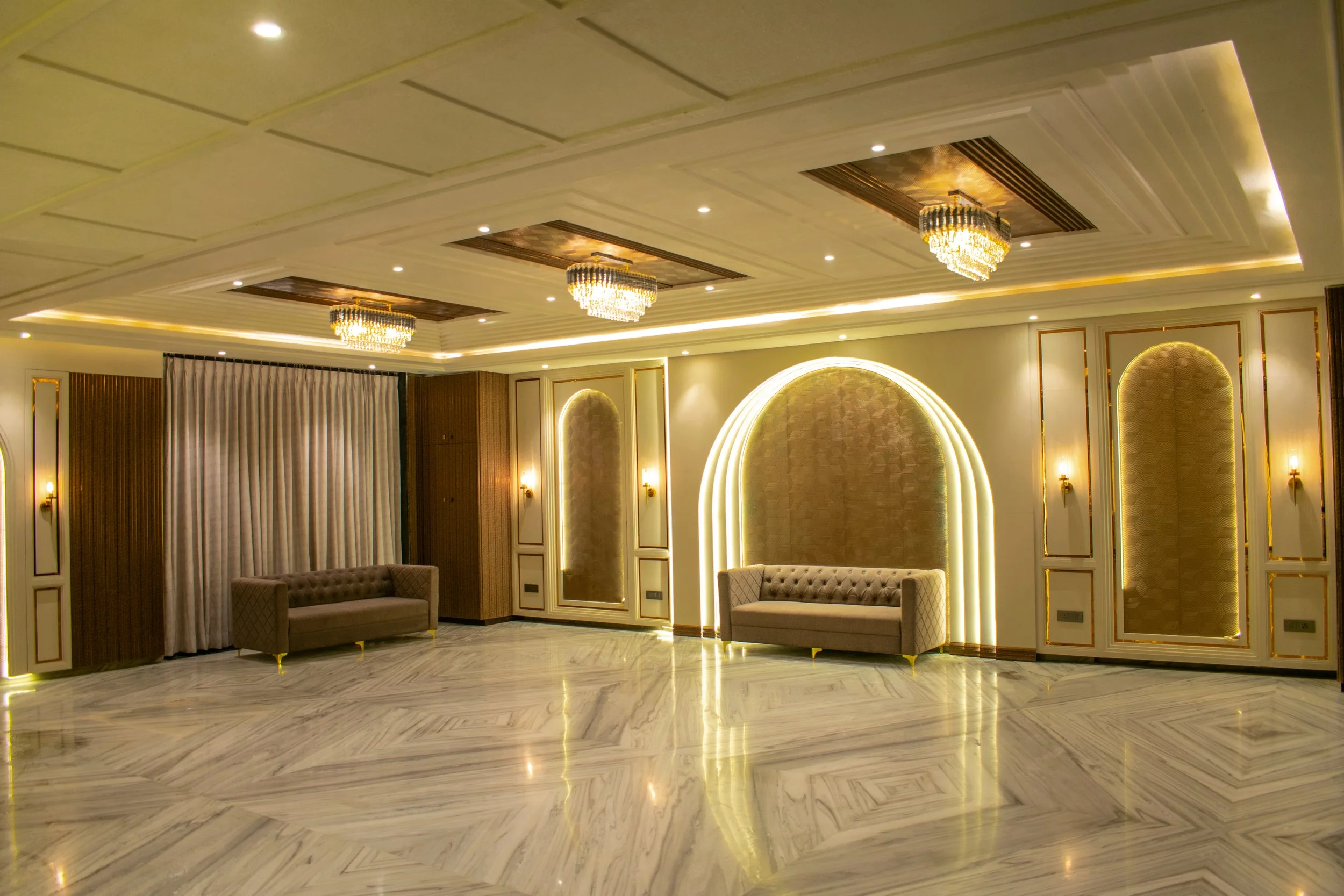 Elegant, well-lit banquet hall with marble floor, two tufted sofas, decorative wall panels, and chandeliers.