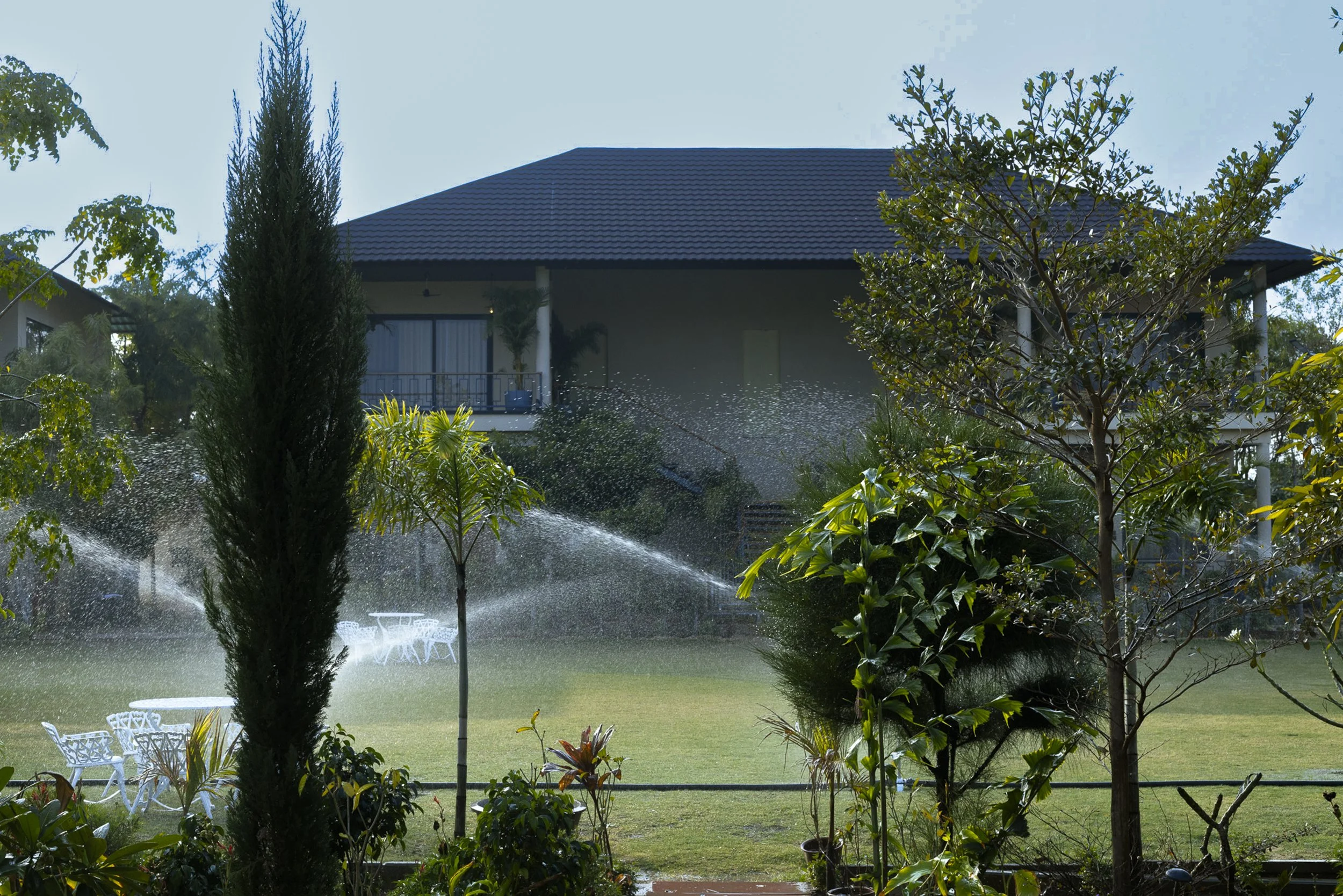 A two-story building with a sign that reads 'YUTORI', surrounded by trees and a black fence, with an Indian flag on the roof and a driveway in front.