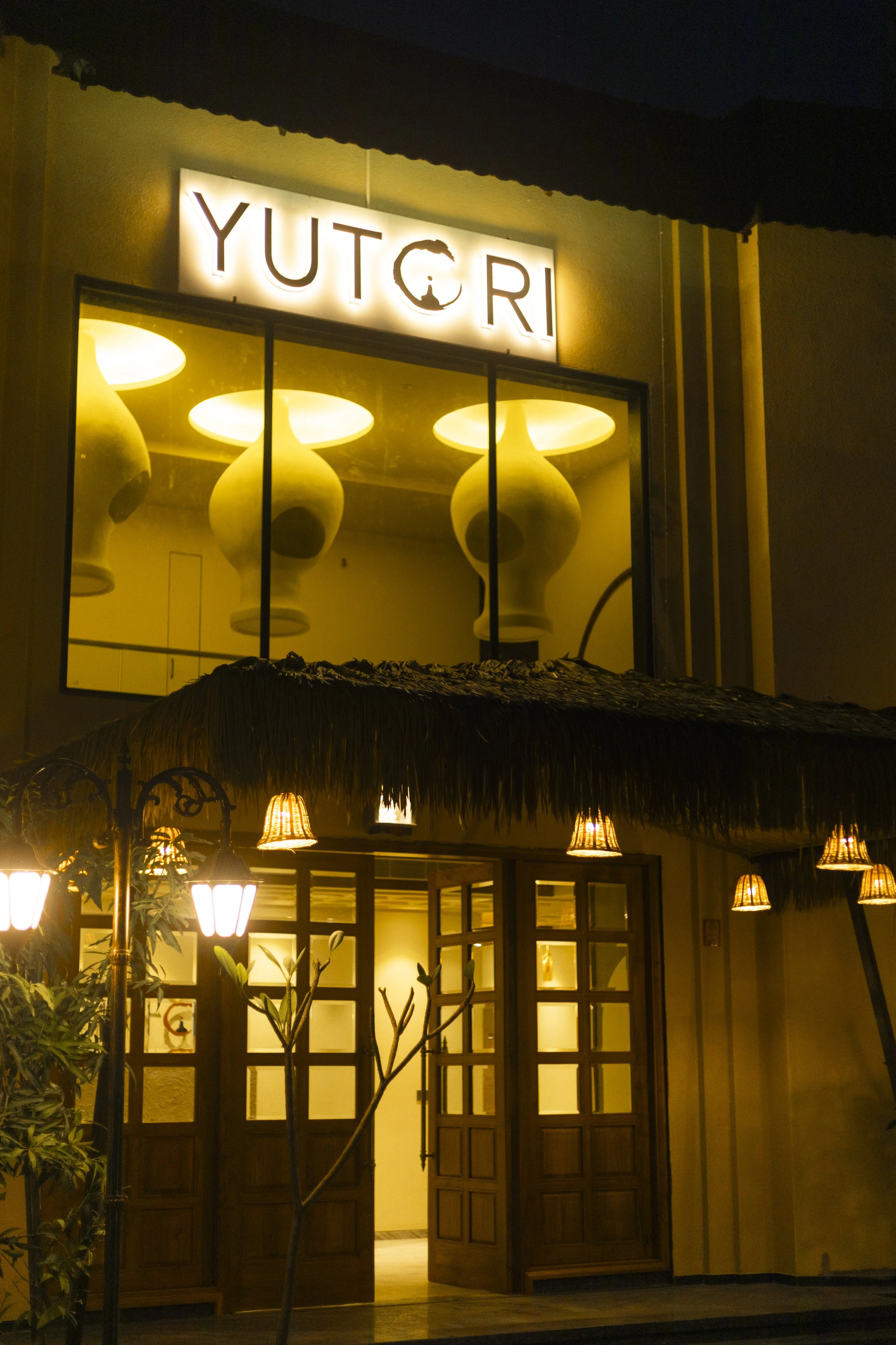 Night view of the entrance to a restaurant or cafe named 'YUTORI' with warm yellow lighting, wooden doors, and hanging lamps outside.