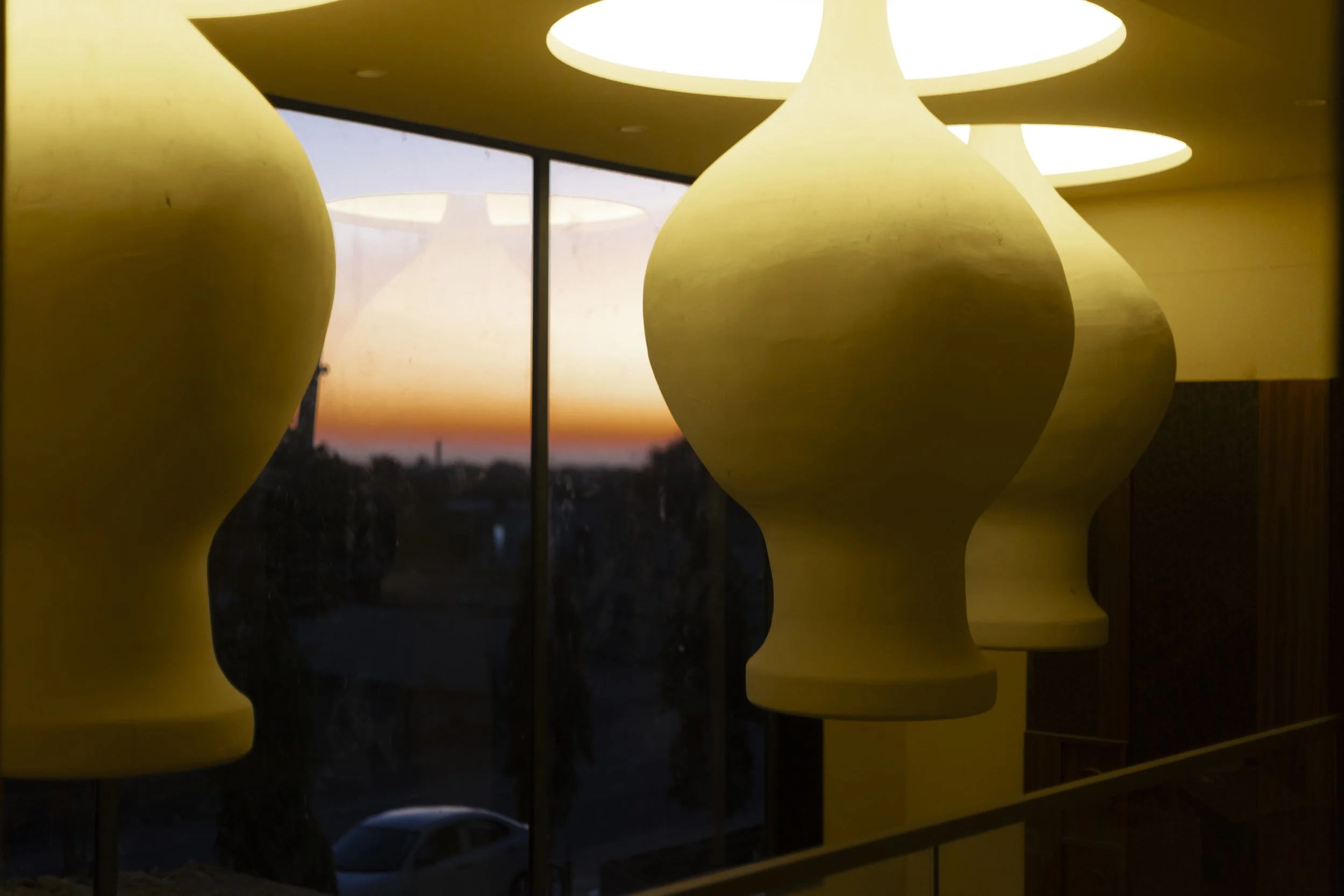 Yellow pendant lights hanging indoors with sunset visible through large windows in the background.