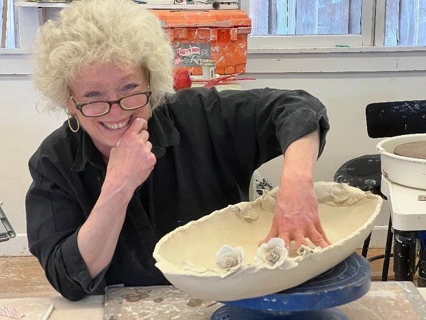 Ceramic artist and total cutie Marianne Cicala with a shallow bowl  with decorative flowers inside, on a pottery wheel in a pottery studio.