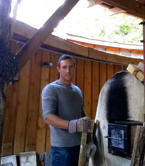 Ceramic artist Galen Sedberry holding a log in preparation to stoke a wood fired kiln full of pottery.