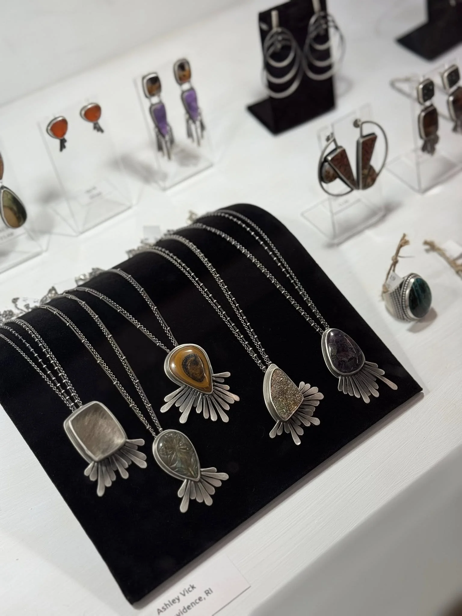 Collection of jewelry including necklaces, rings, and earrings with various stones displayed on a black stand and clear acrylic holders.