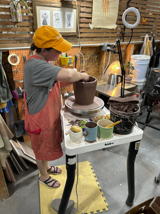 Ceramic artist Allie Stack shaping a large clay pot on a pottery wheel in a workshop