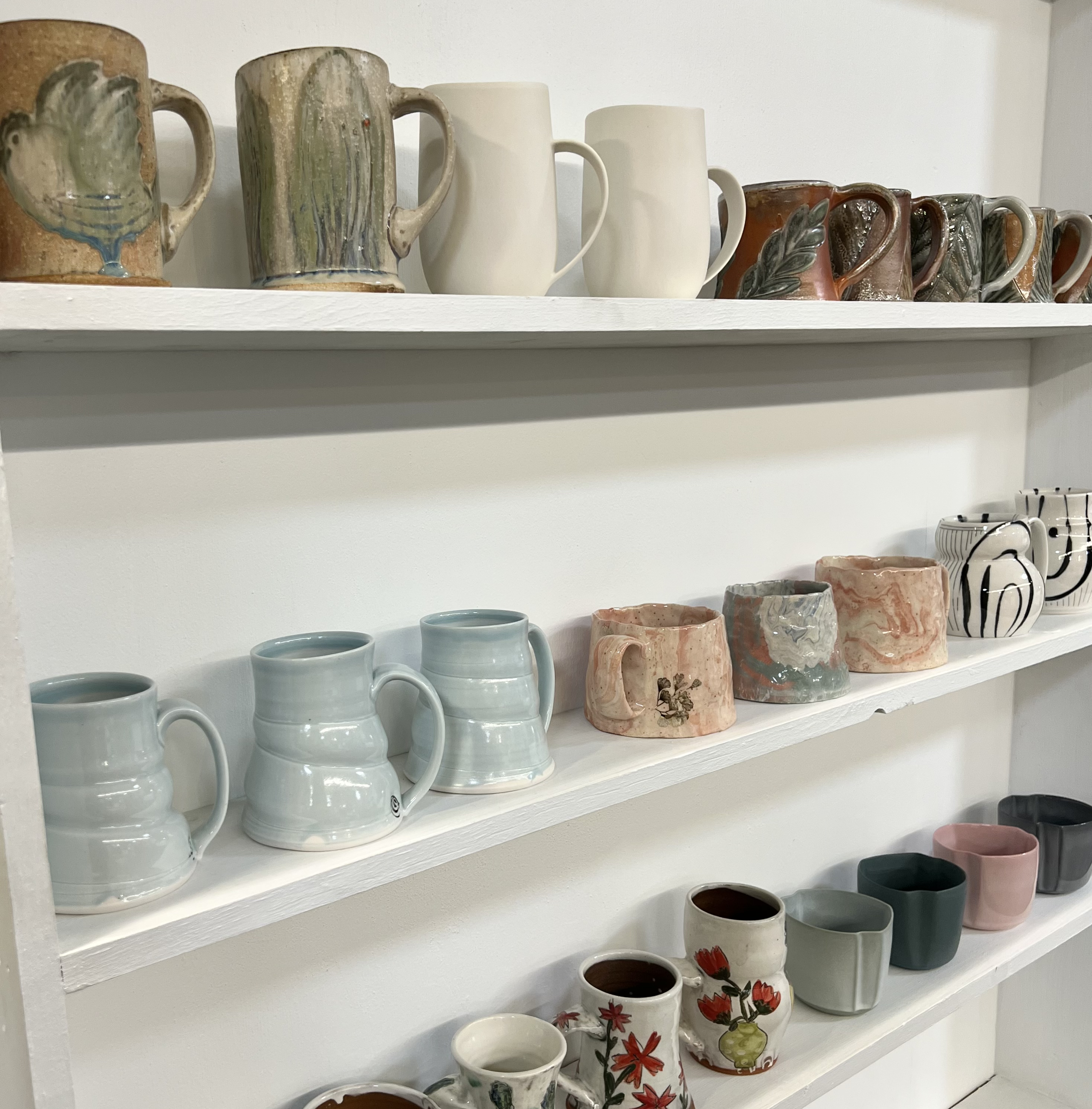 White shelves displaying various ceramic mugs and cups in different colors and patterns.