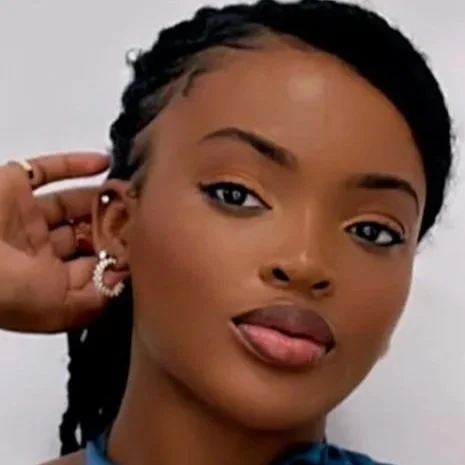 Close-up of a woman with braided hair and earrings, looking at the camera with her tongue slightly out.