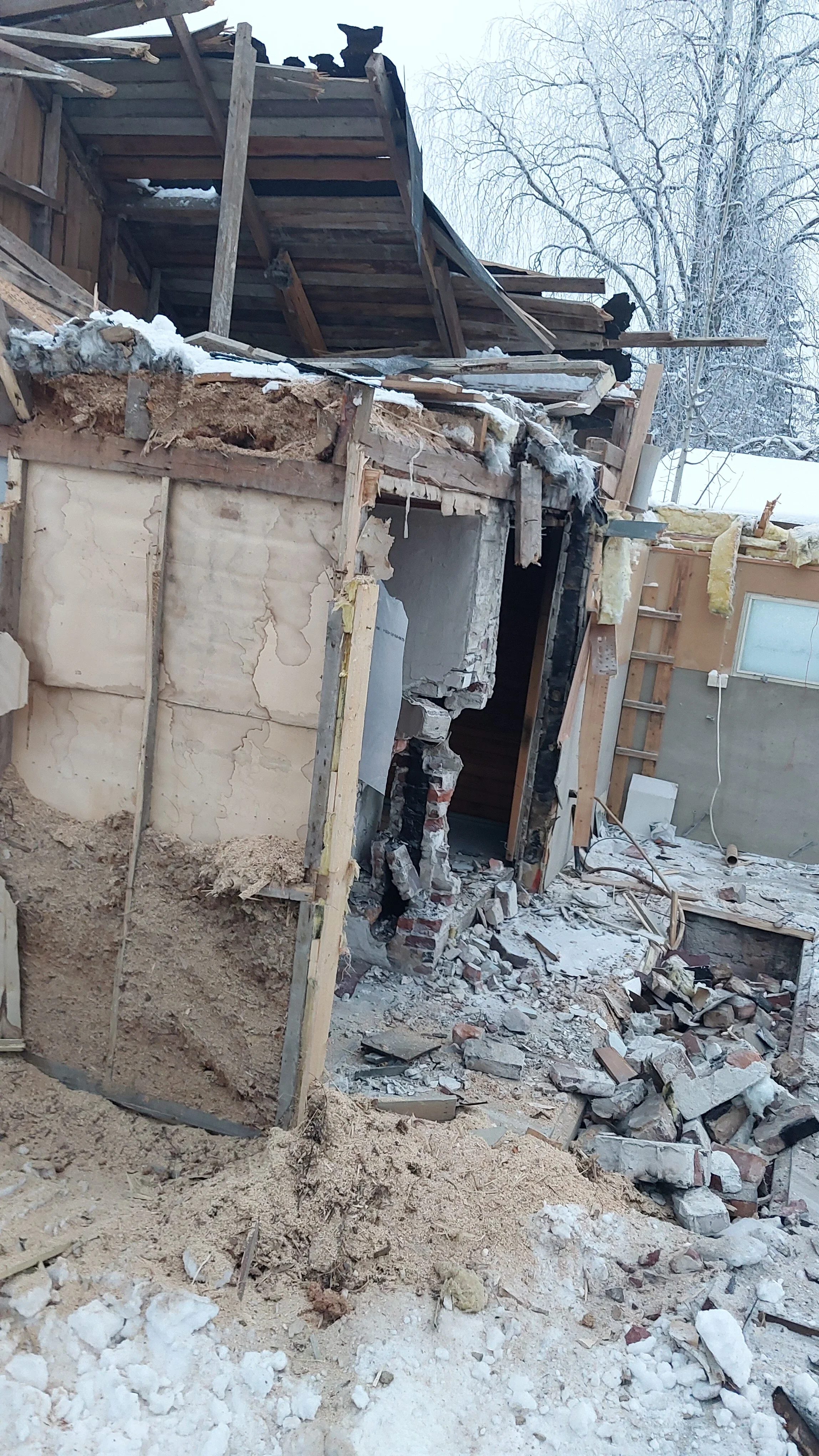 Osittain purettu rakennus jossa on romahtanut seinä ja katto, maassa purkujätettä ja lunta.