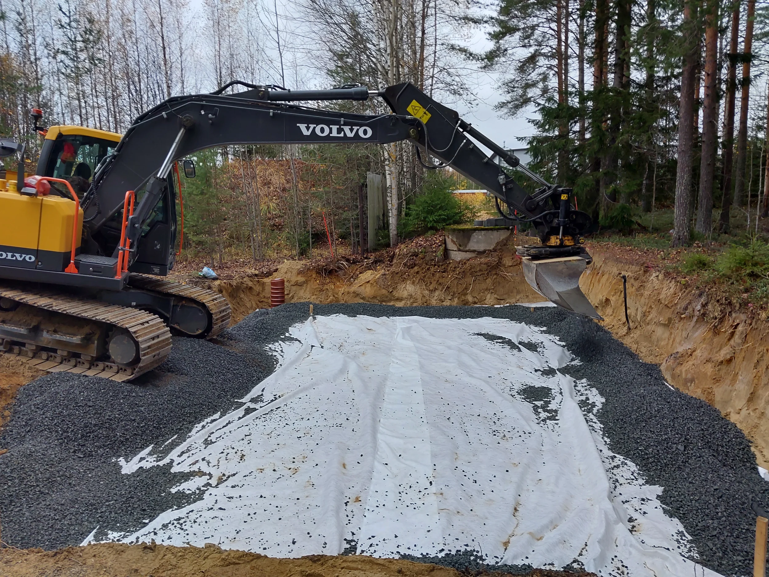 Salaojaremontti, jossa kaivinkone levittää soraa osittain näkyvän suojakankaan päälle.