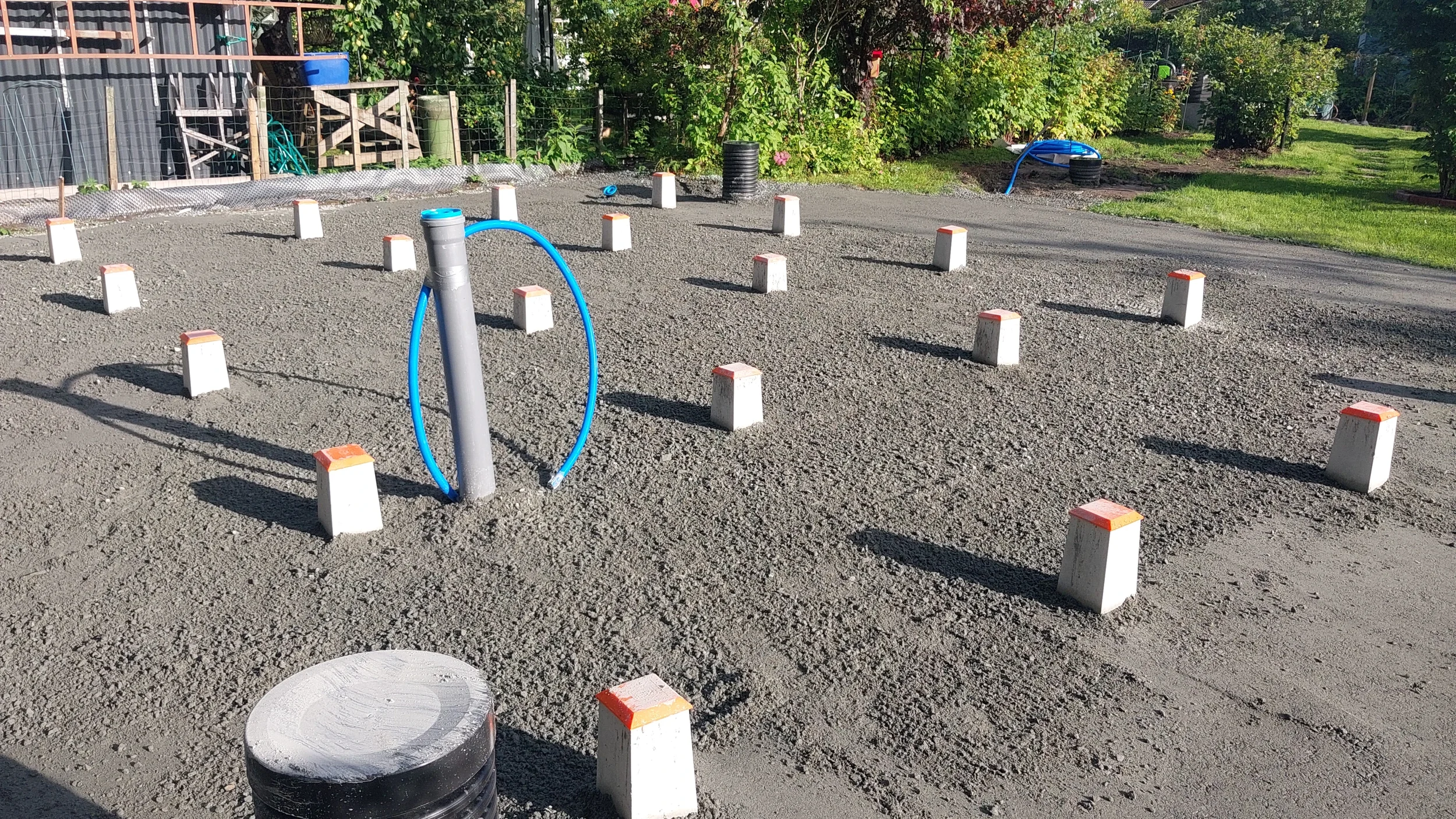 Työmaa, jossa on mökin pilariperustukset. Ympärillä kasvillisuutta ja pihamaisemaa.