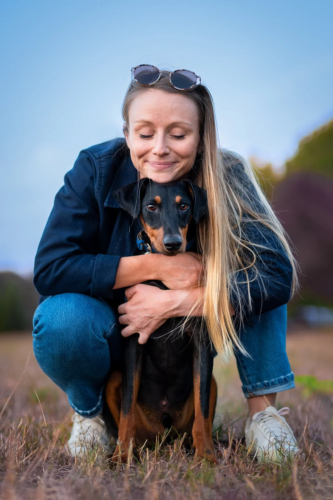 Une femme souriante serre dans ses bras un chien noir et feu lors d'une promenade en plein air au crépuscule. 