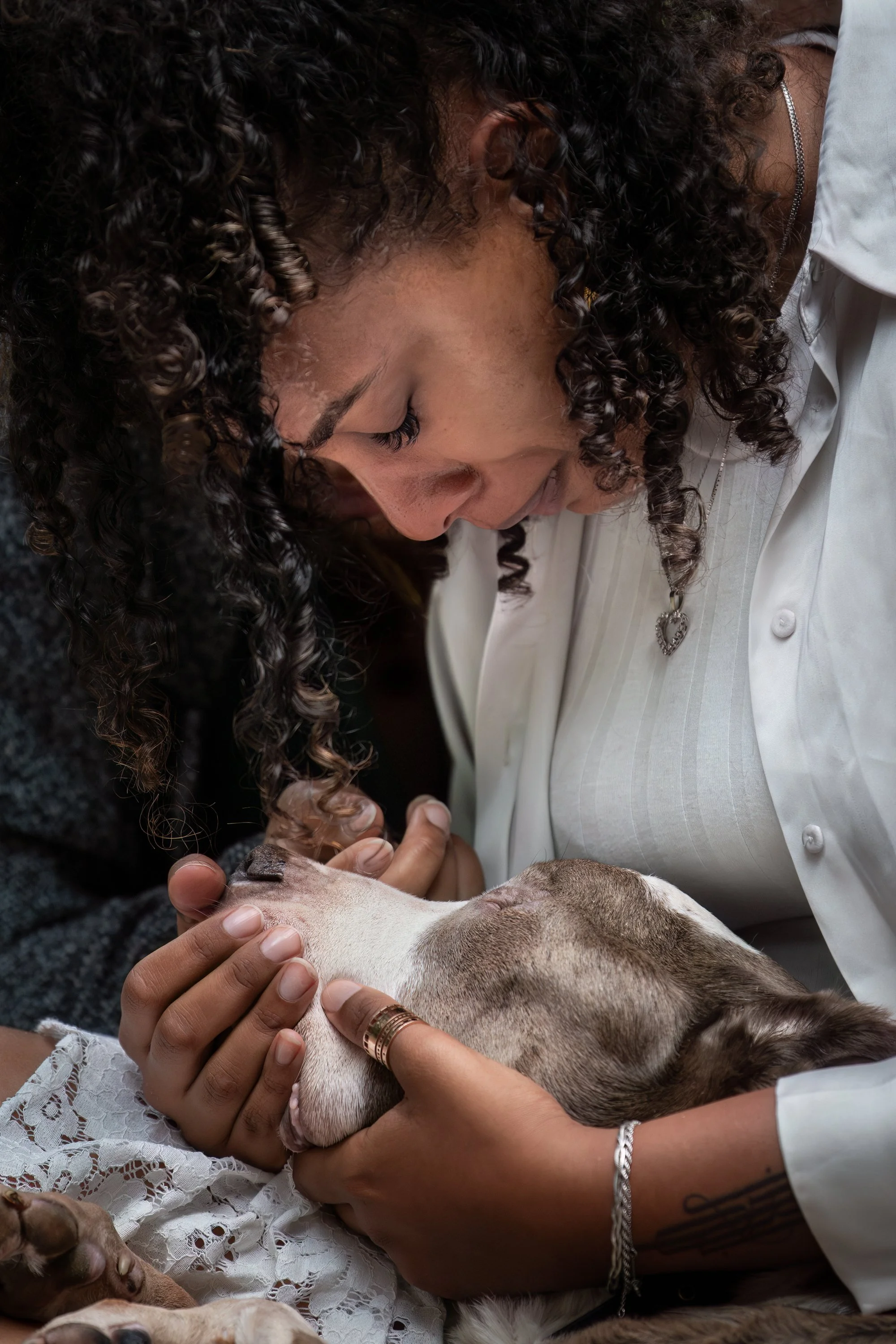 Deux femmes proches, une avec des cheveux bouclés, caressent la tête d'un chien allongé sur leurs genoux, créant une scène tendre et affectueuse.