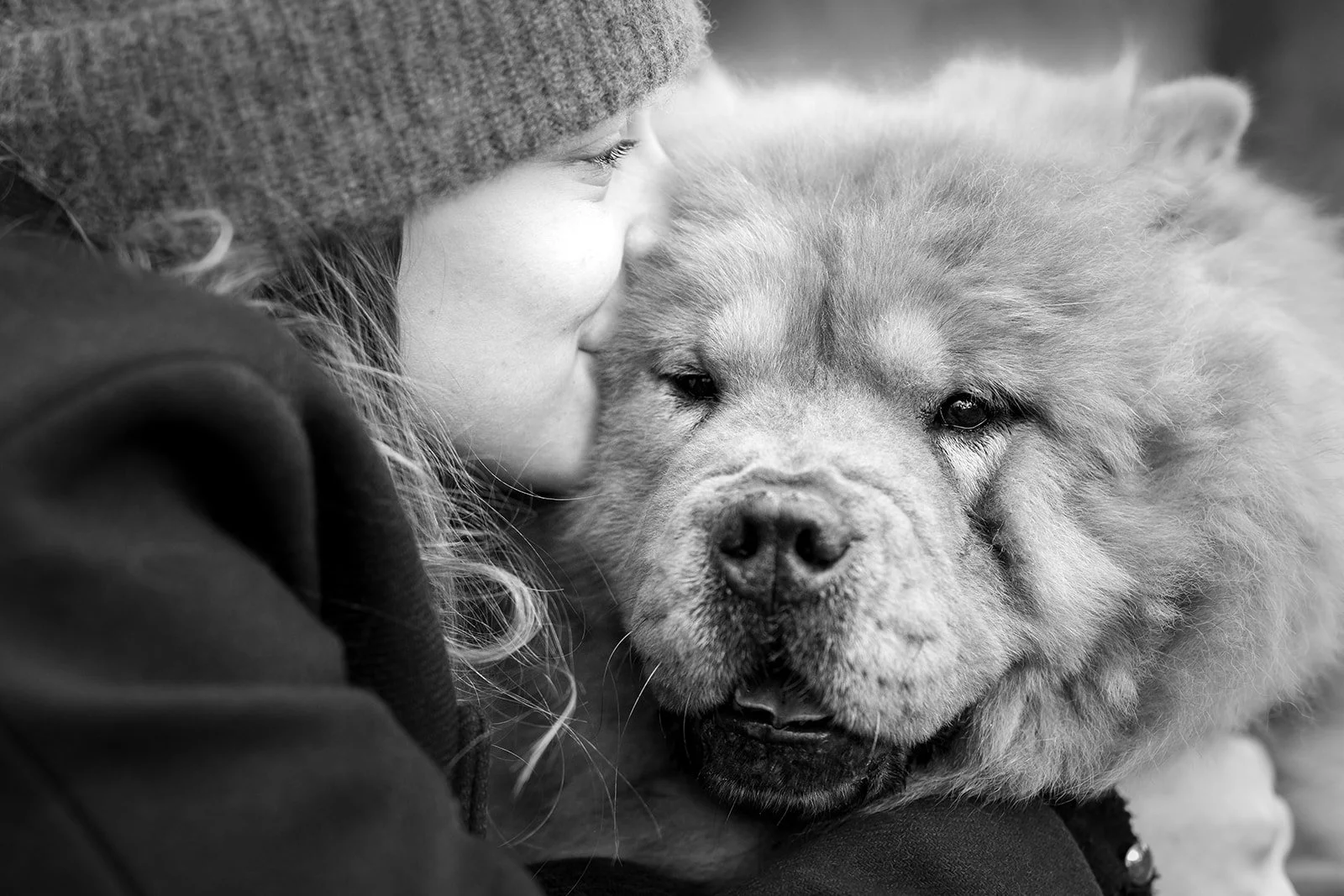 Un portrait rapproché d'une femme embrassant un chien chowchow. Photo noir et blanc.