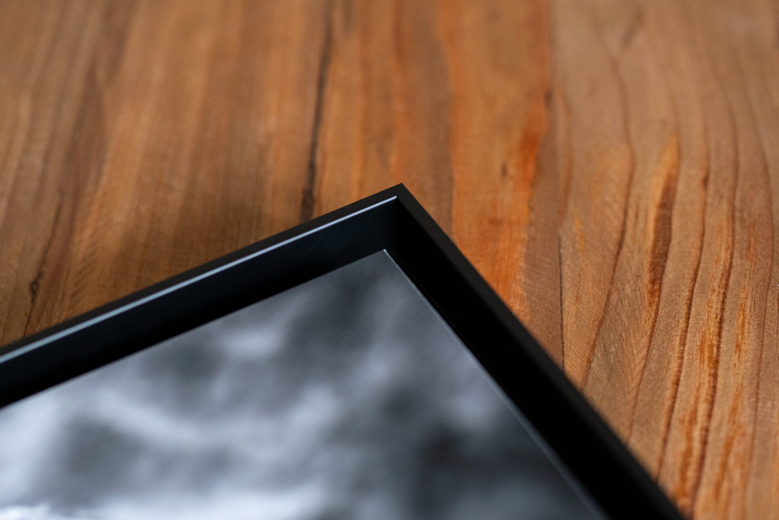 Coin supérieur gauche d'un cadre photo noir, posé sur une surface en bois.