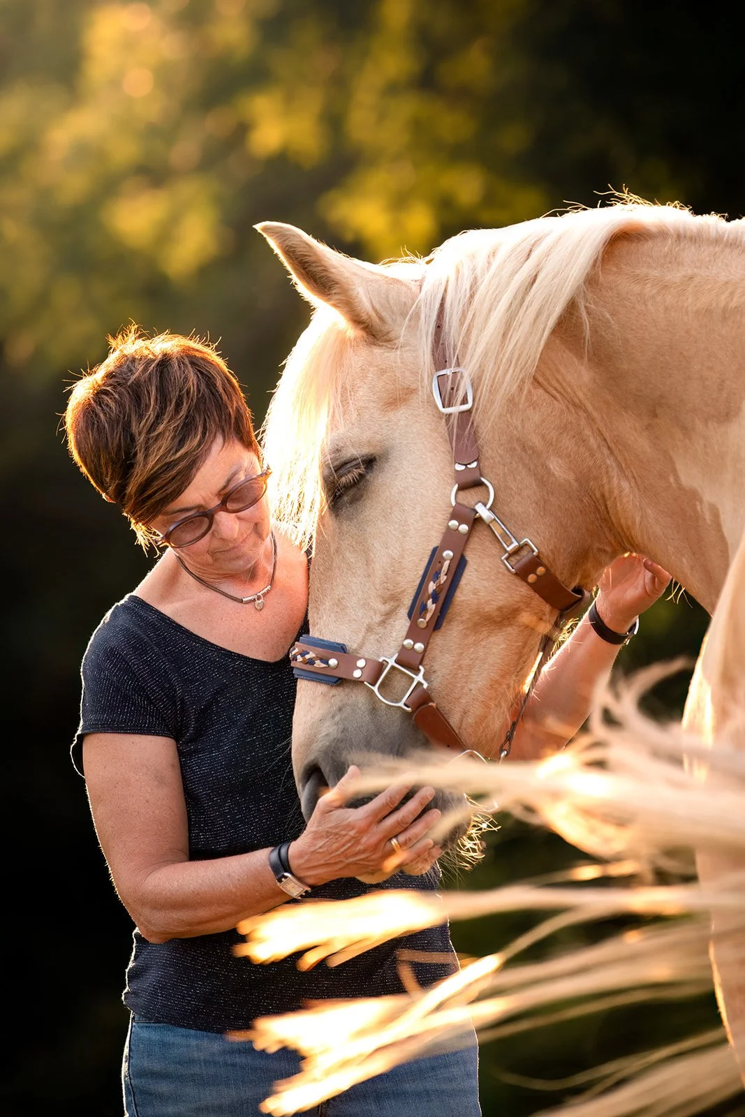 Une femme regarde et câline tendrement un cheval palomino lors d'un coucher de soleil en extérieur.