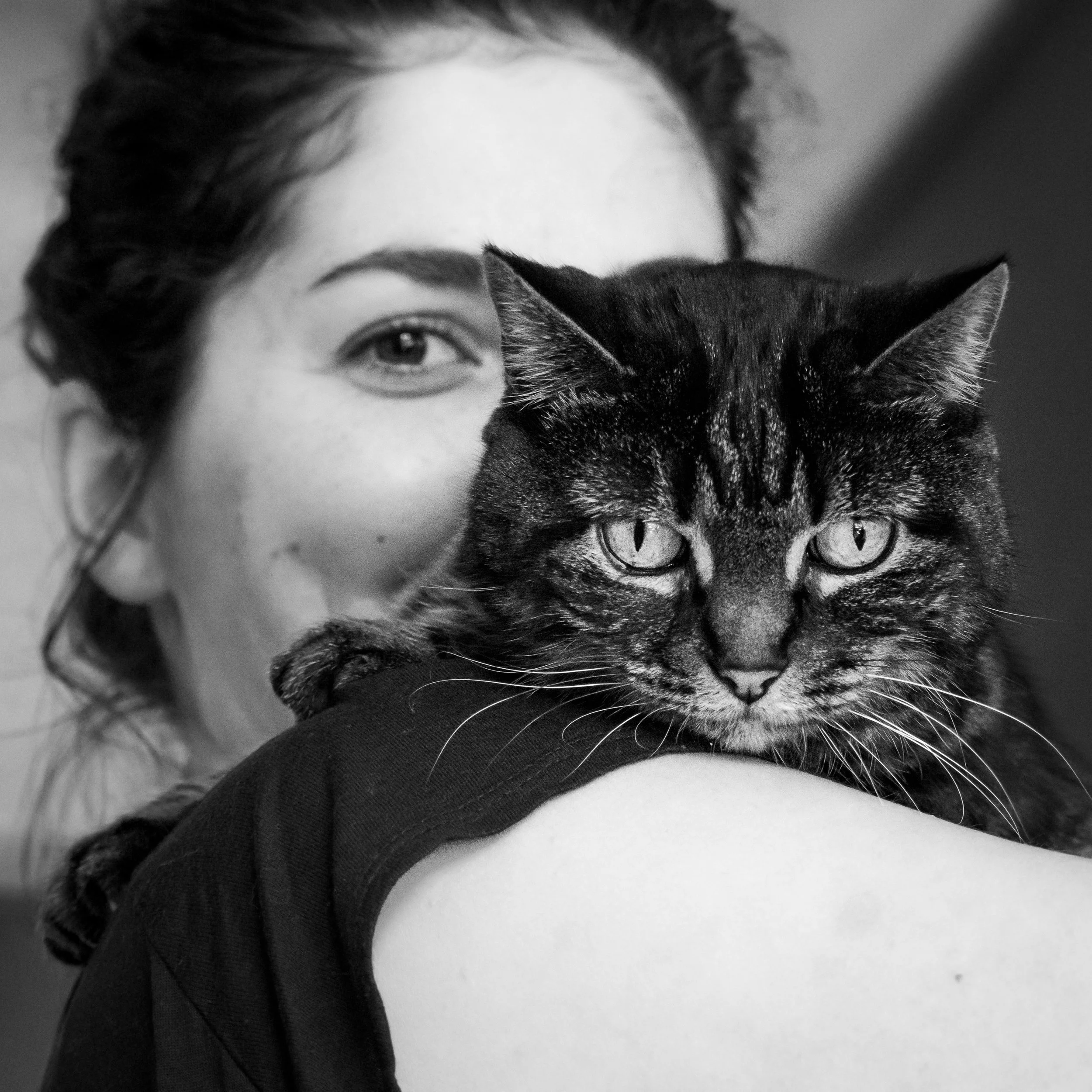 Une femme tient un chat noir tacheté sur son épaule. Le plan est un portrait très serré. Photo noir et blanc.