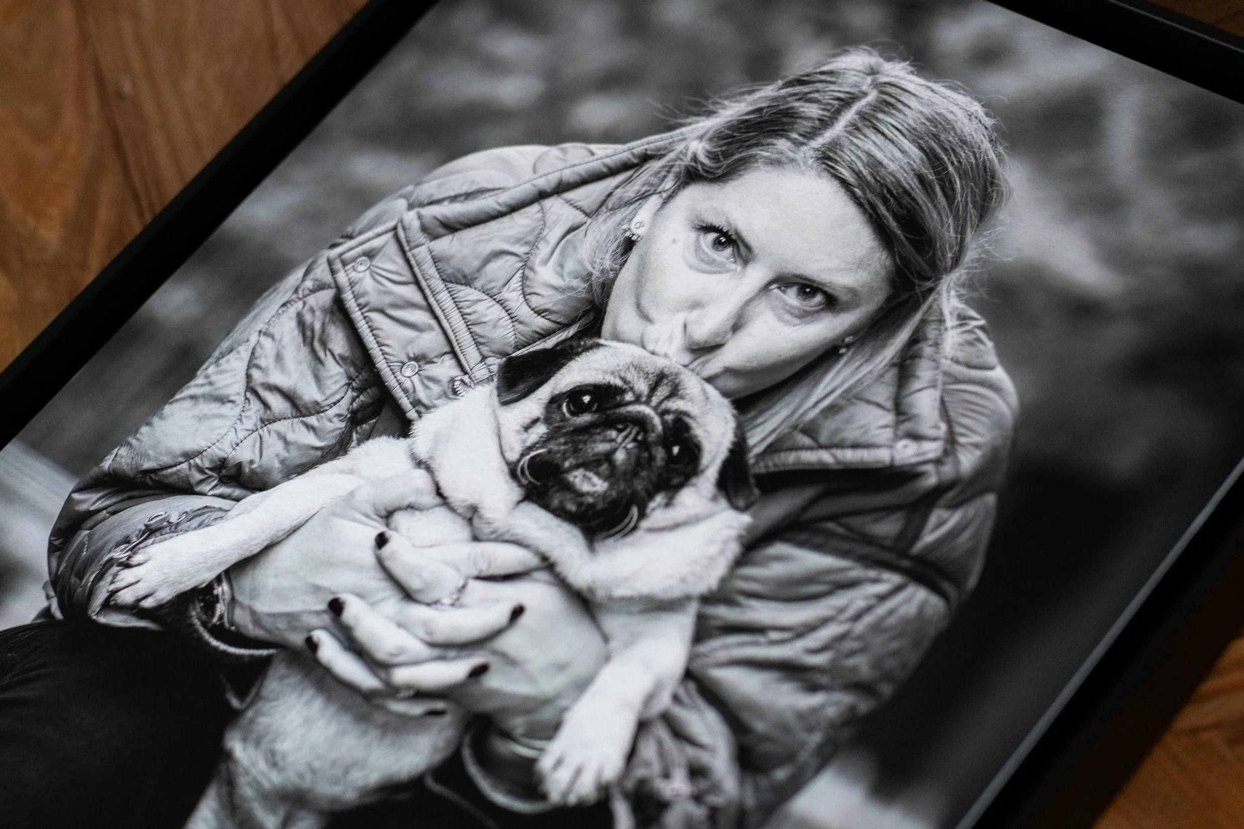 Une femme avec des cheveux longs tenant un chien carlin sable. La photo est en noir et blanc.