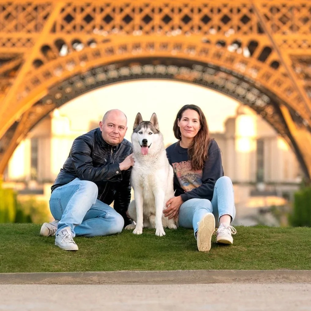 Un couple avec un chien husky pose assis devant la tour Eiffel à Paris au lever du soleil. 
