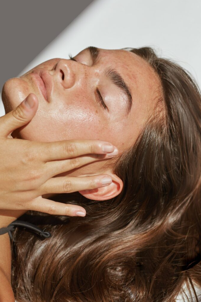 Close-up of a woman receiving a facial massage, lying down with her eyes closed.