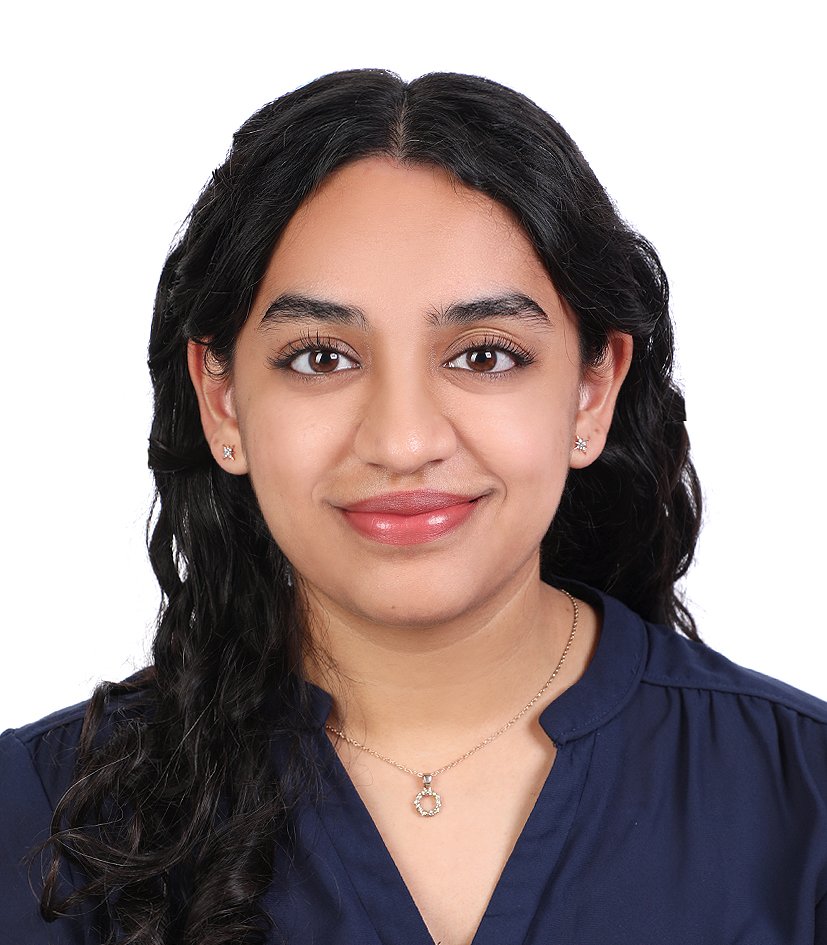 Portrait of a woman with dark wavy hair, wearing a navy blouse and a necklace, smiling against a white background.