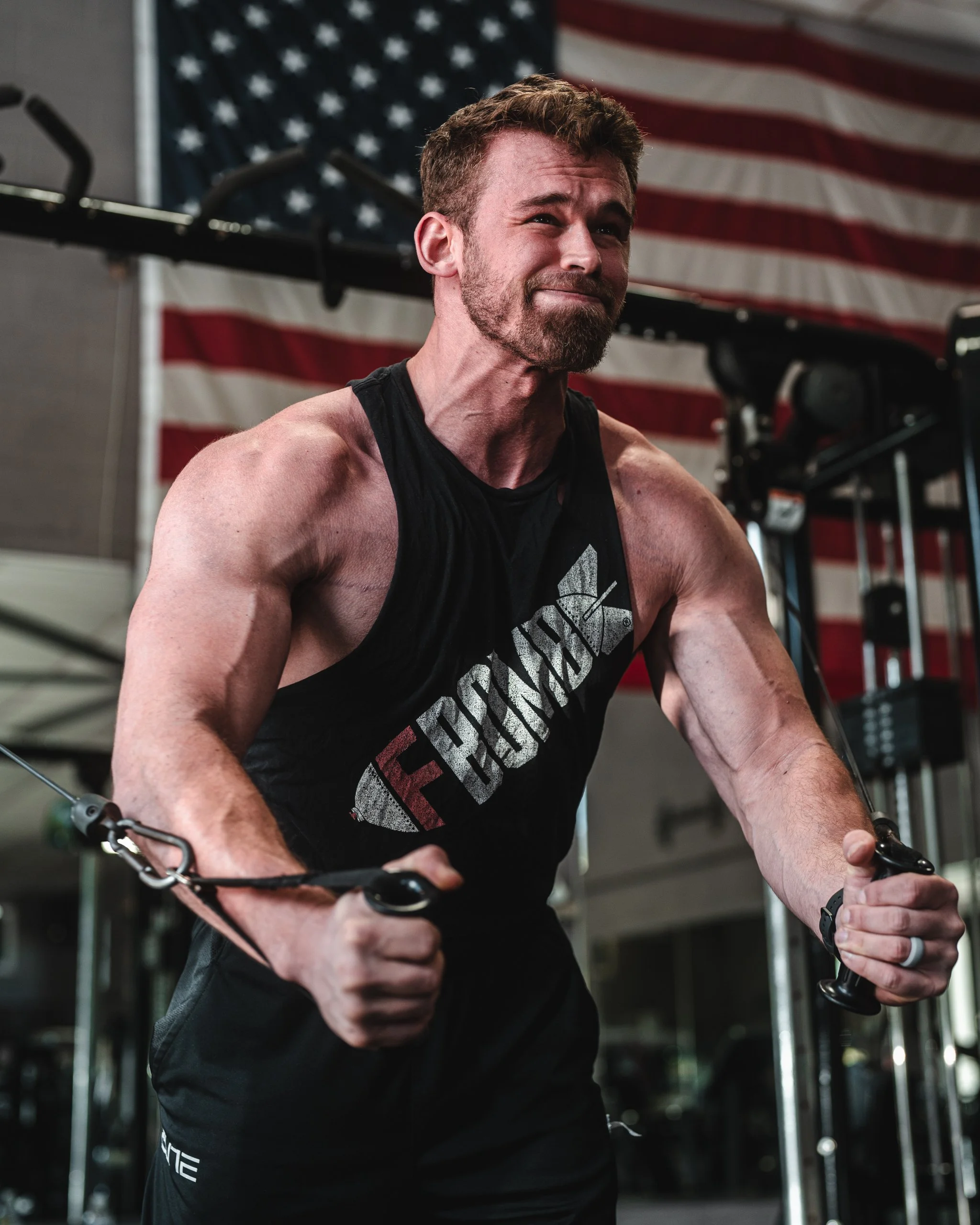 Man performing a cable chest fly workout in a gym with an American flag in the background.