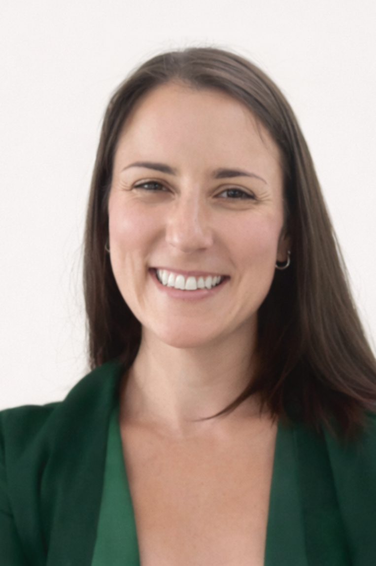A smiling woman with shoulder-length brown hair, wearing a green blazer, taking a selfie against a plain white background.