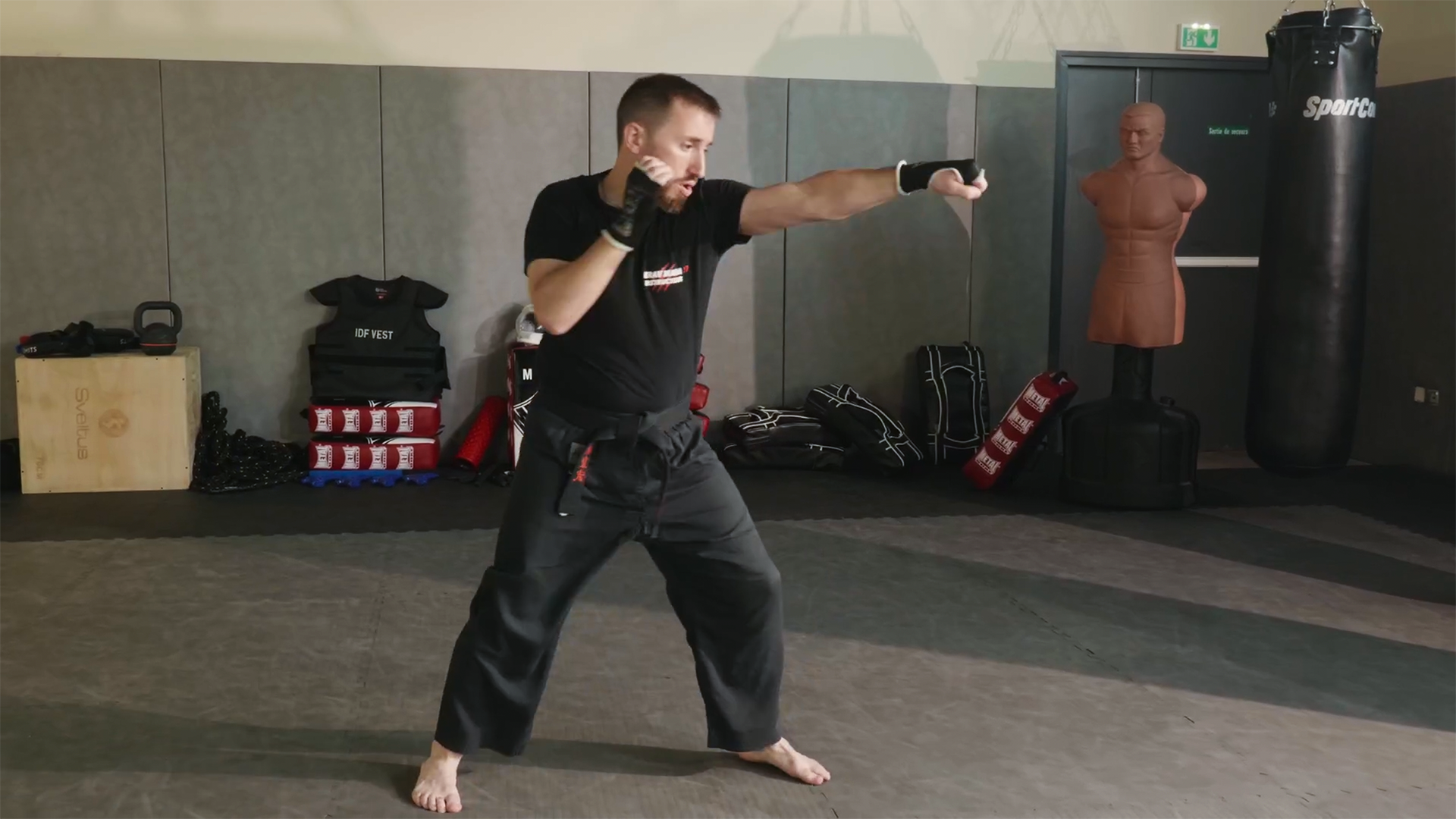 Plan pied de Guillaume, en tenue de sport, qui pratique la boxe seul dans une salle d'entraînement, lançant un coup de poing.