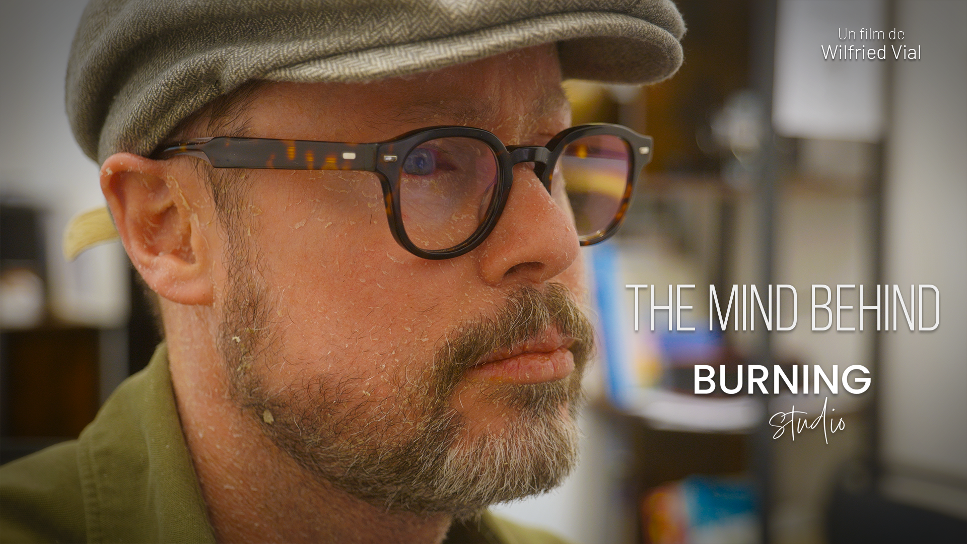 Affiche du film The Mind Behind. Portrait en gros plan de Manuel Brule, photographe et fondateur du Burning Studio, casquette et lunettes rondes, Titre du film en anglais sur l'image, et en haut à droite : "Un film de Wilfried Vial".