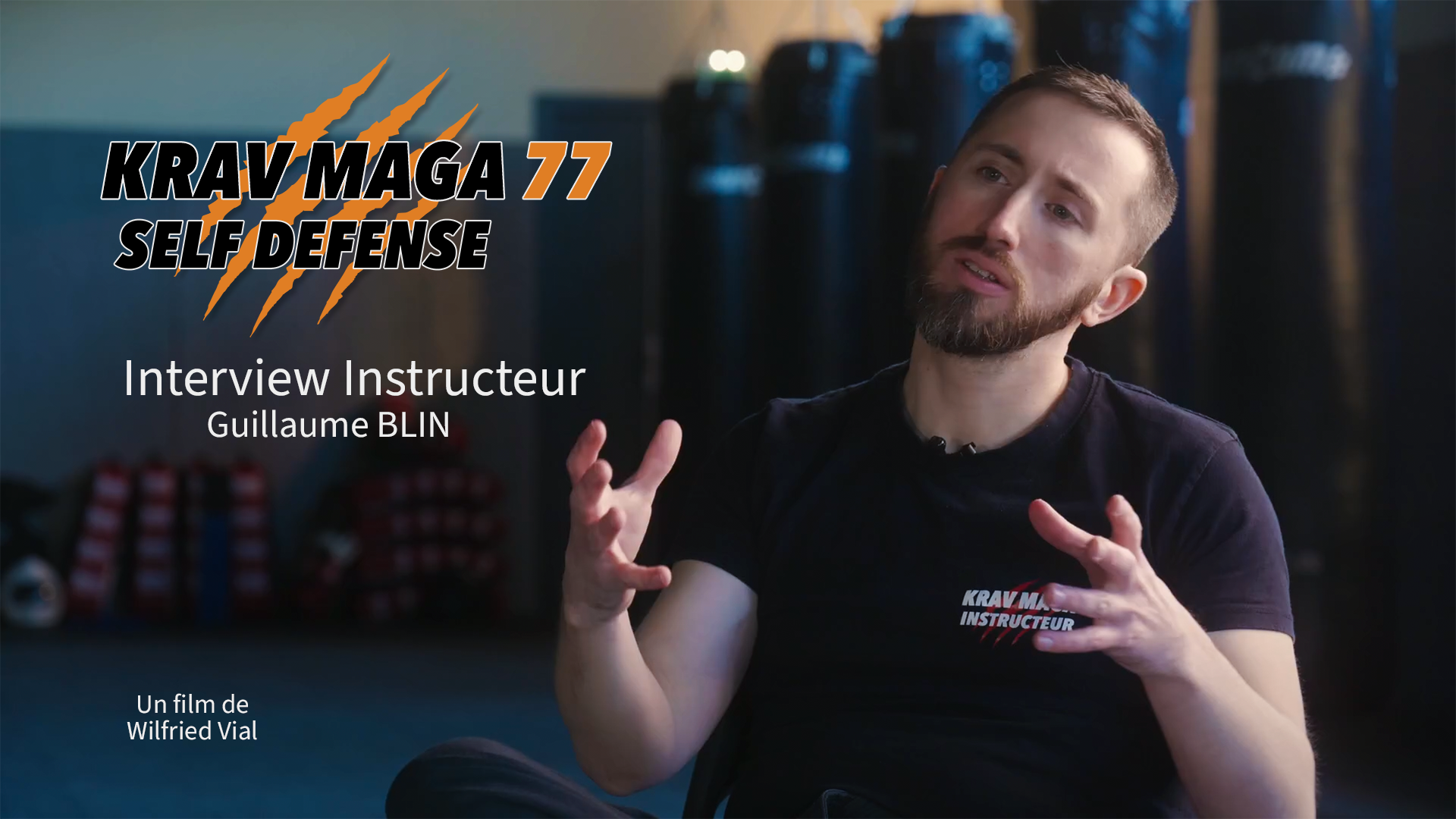 Affiche de la vidéo de l'interview de Guillaume Blin, instructeur de krav maga. Image de Guillaume, en T-shirt à l'effigie du club, parlant dans un gymnase avec des sacs de boxe en arrière-plan.