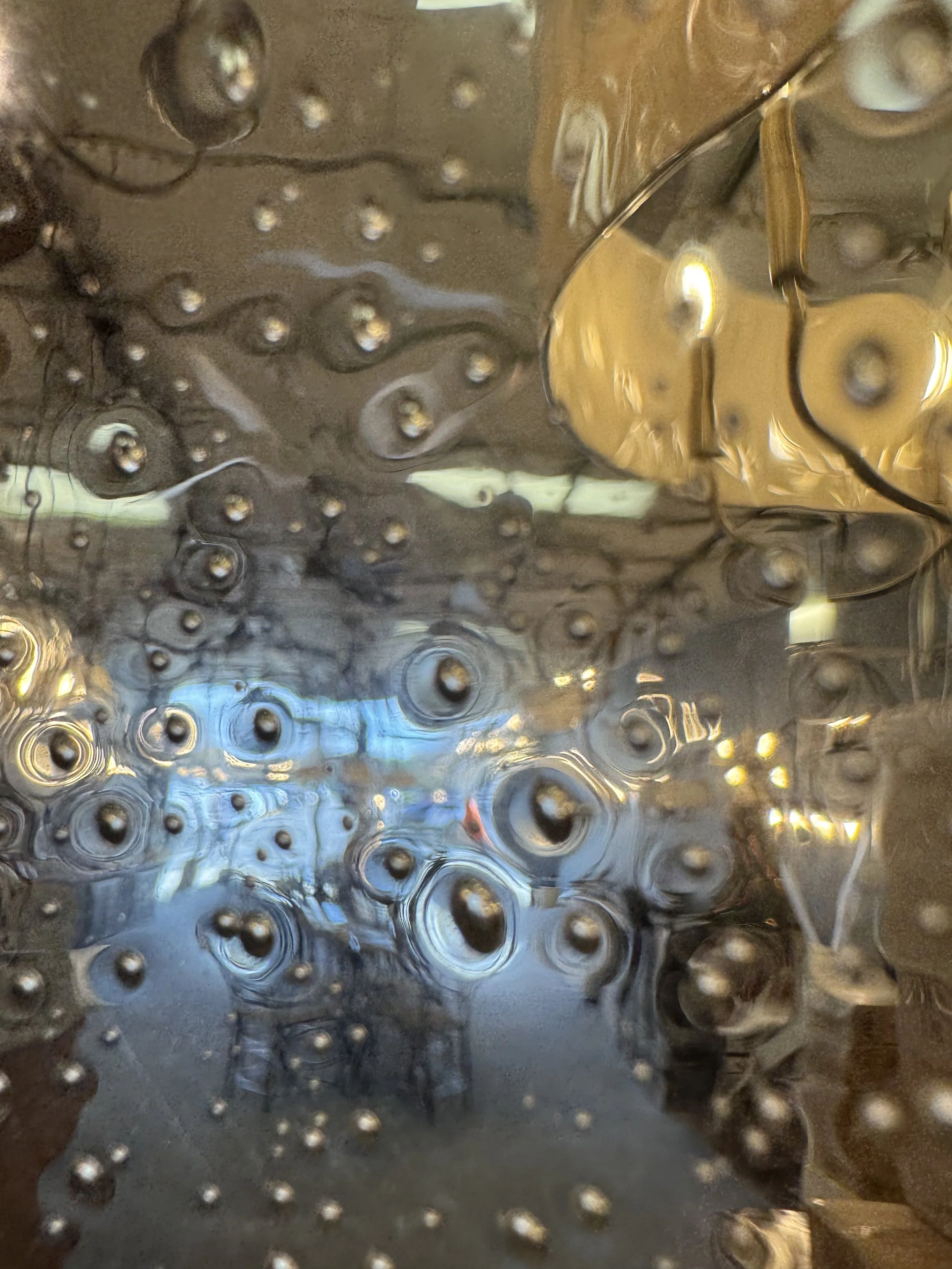 Close-up of a glass surface with water droplets and streaks, creating a textured, abstract pattern.