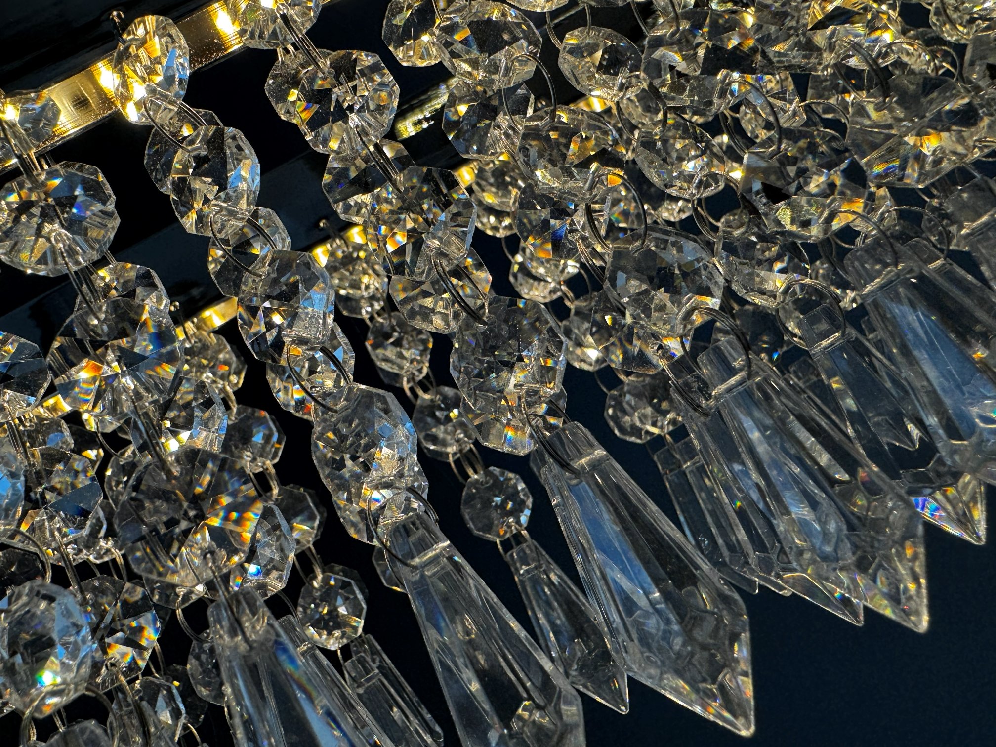 Close-up of a crystal chandelier with multiple hanging faceted crystals reflecting light against a dark background.