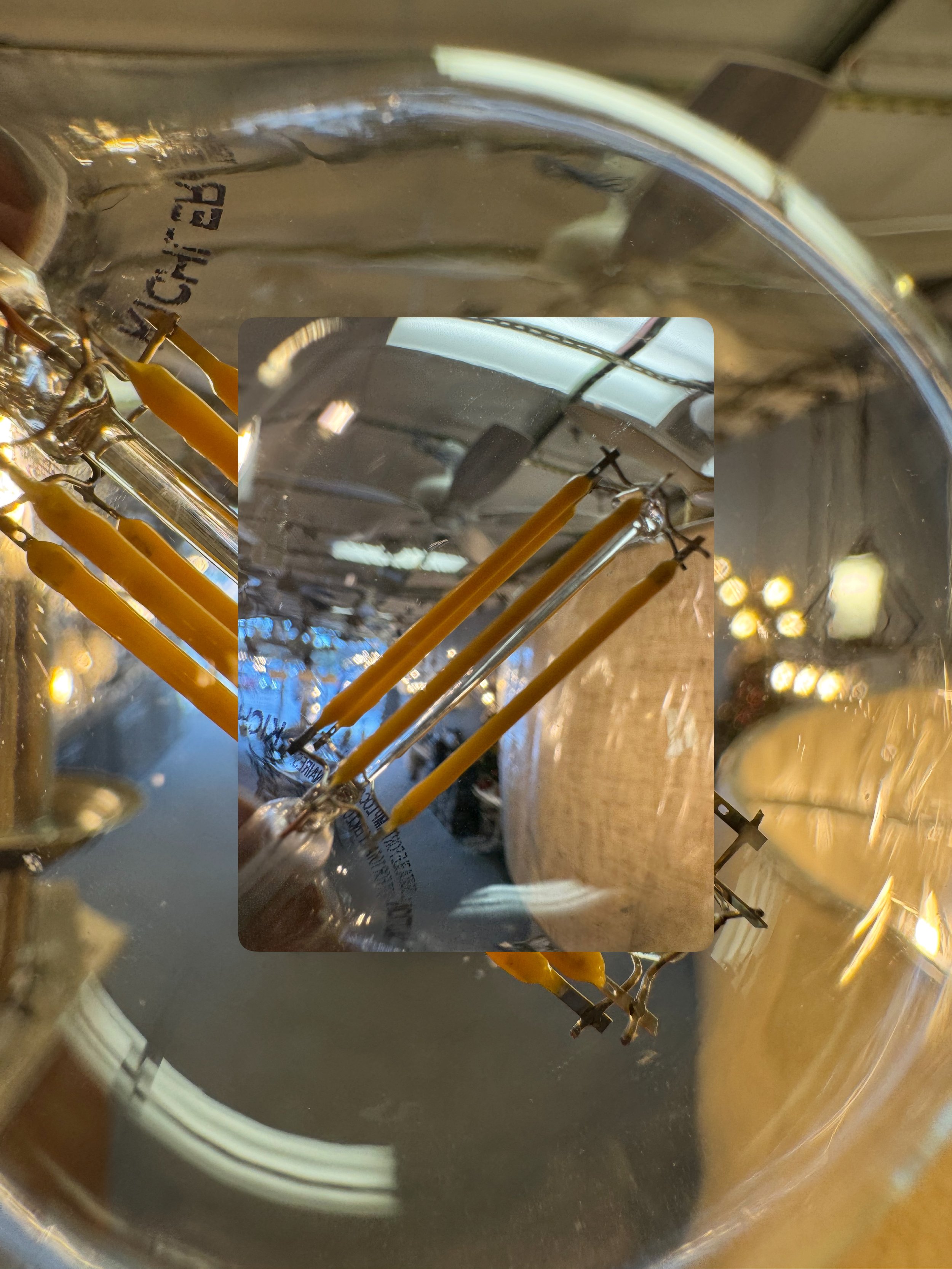 Close-up of a glass light fixture with yellow candles inside, reflecting the surrounding ceiling lights and interior space.