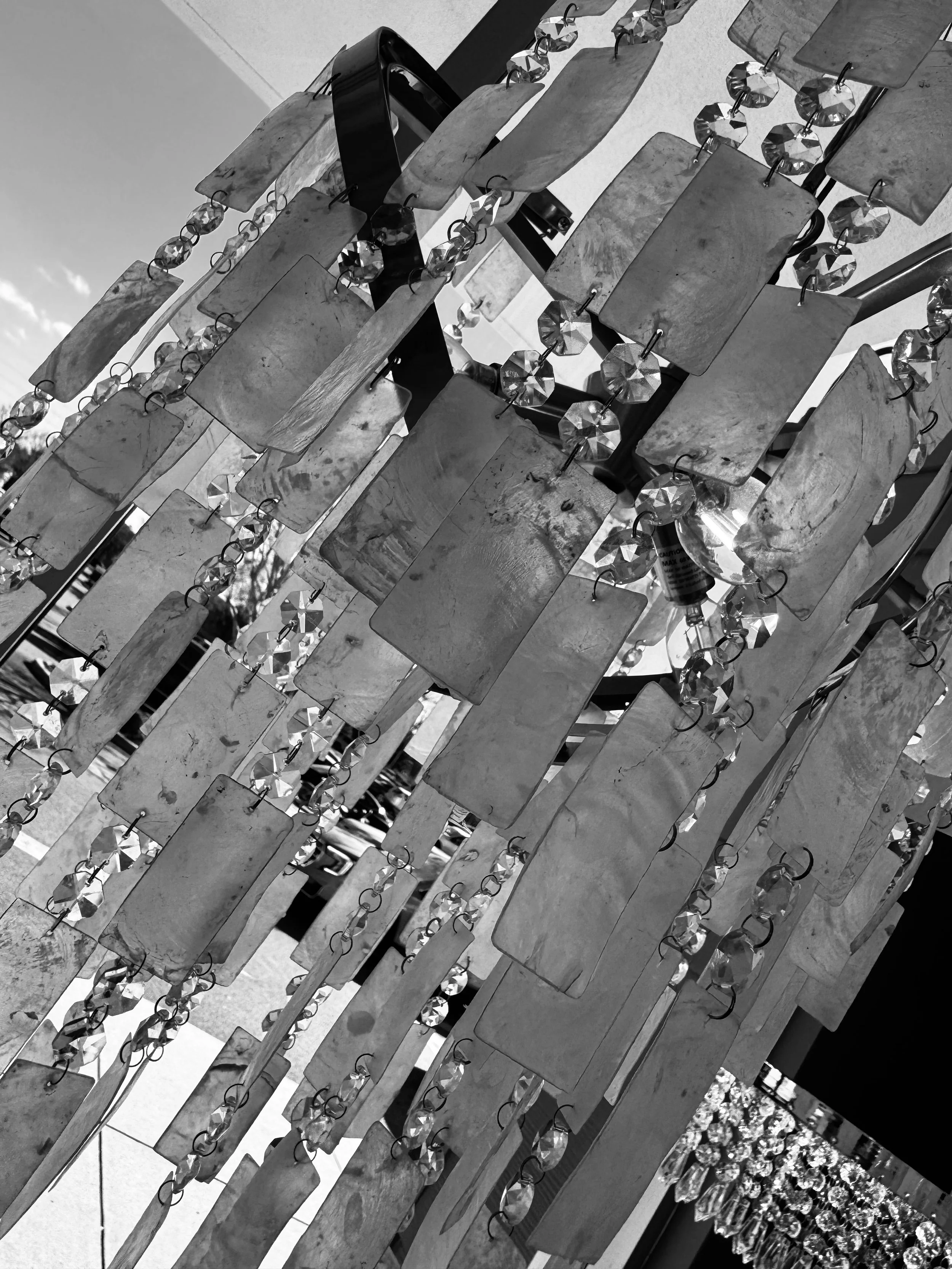 Black and white photo of a decorative hanging ornament with rectangular metallic pieces and faceted crystal beads, part of a larger display.