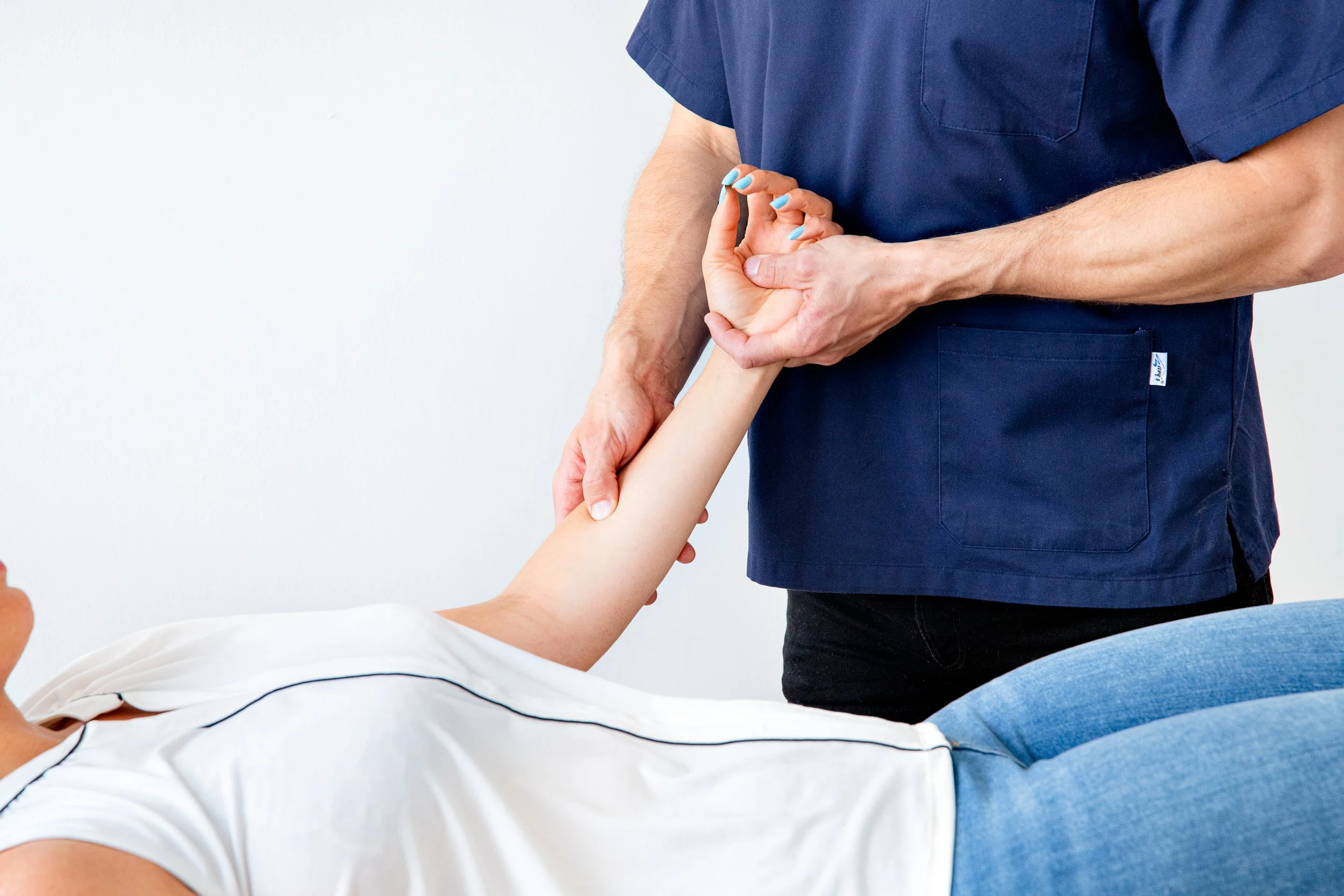 A person lying on a medical examination table holding hands with a healthcare professional in navy scrubs, who is providing support or conducting an examination.