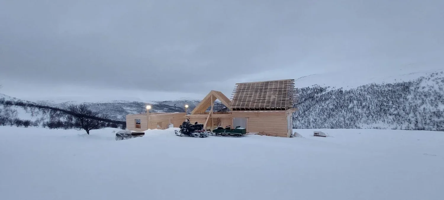 Kuvassa rakennus täydessä rakennusvaiheessa lumisella maaseudulla, lumen ollessa syvä, ja taivaalla pilvinen sää. Rakennusliike Utsjoki (Construction company Utsjoki)
Rakennuspalvelu Inari (Construction service Inari)
Urakoitsija Ivalo (Contractor)