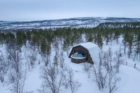 Lunta peittynyt mökki metsän keskellä talvisessa maisemassa.
