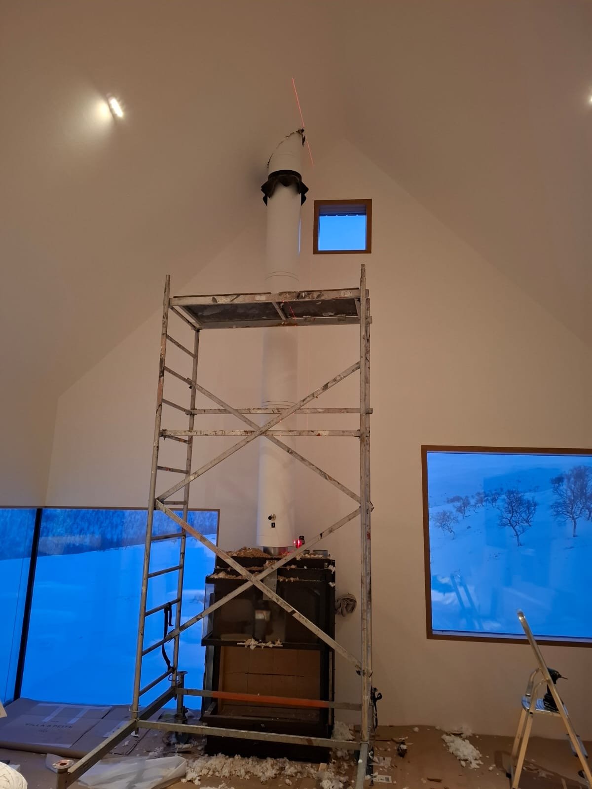 Sisätiloissa rakennustyömaa, keskellä teline ja putki, ikkunat ja luminen maisema näkyvät taustalla.
